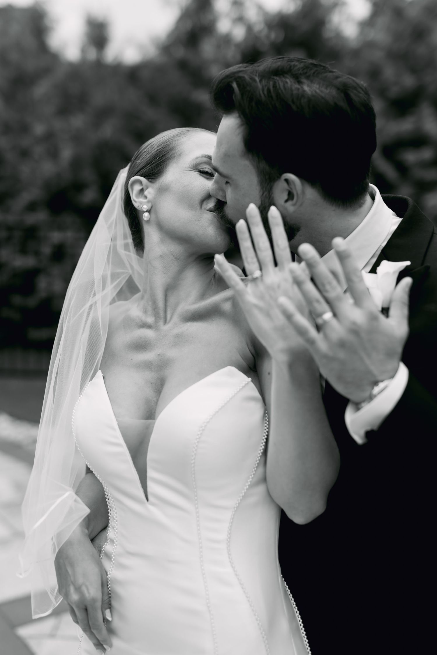 Black and white romantic photo of bride and groom nearly kissing while showing off wedding rings.