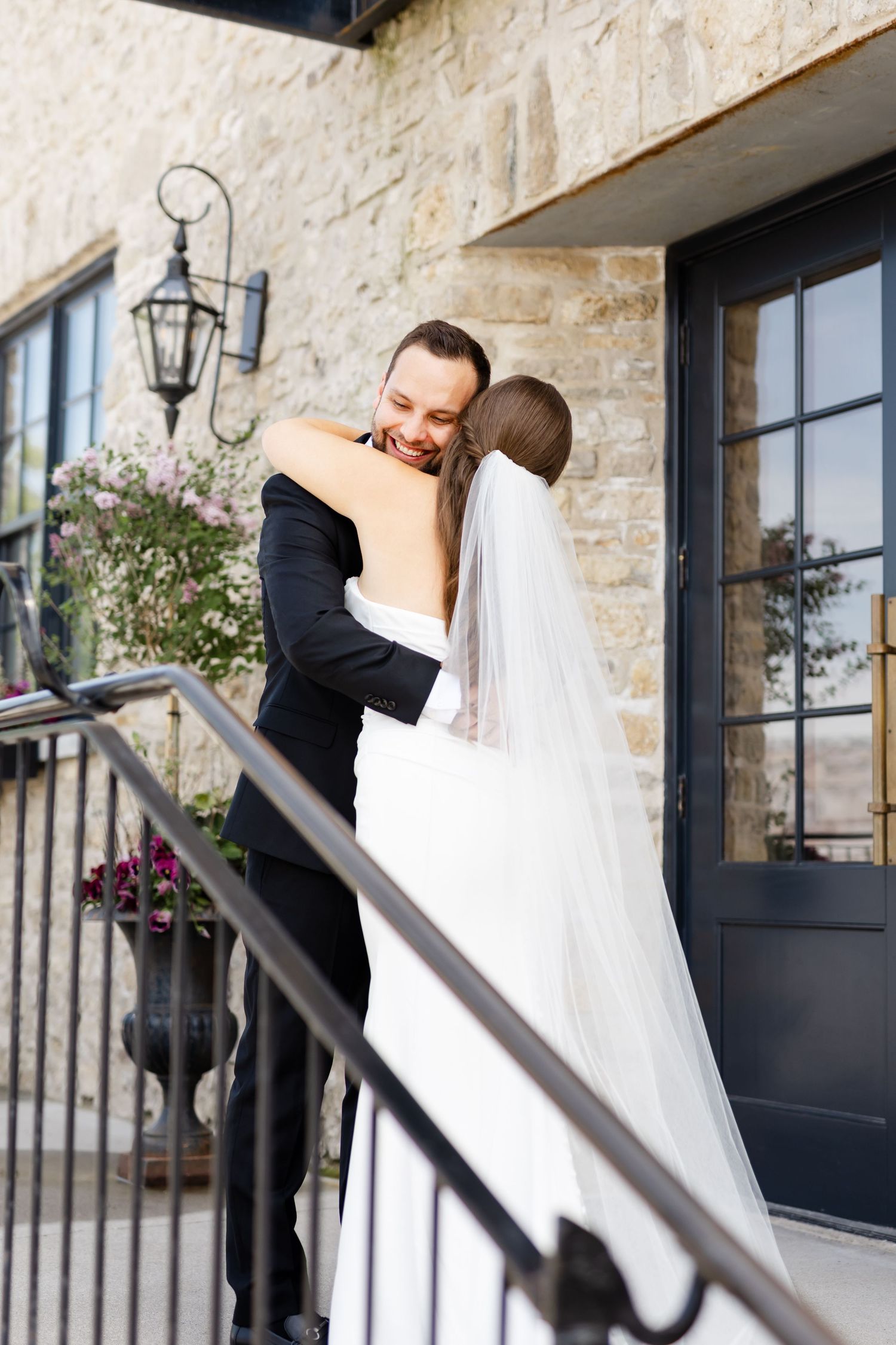 Bride and groom share a joyful embrace on stone steps outside a rustic wedding venue.