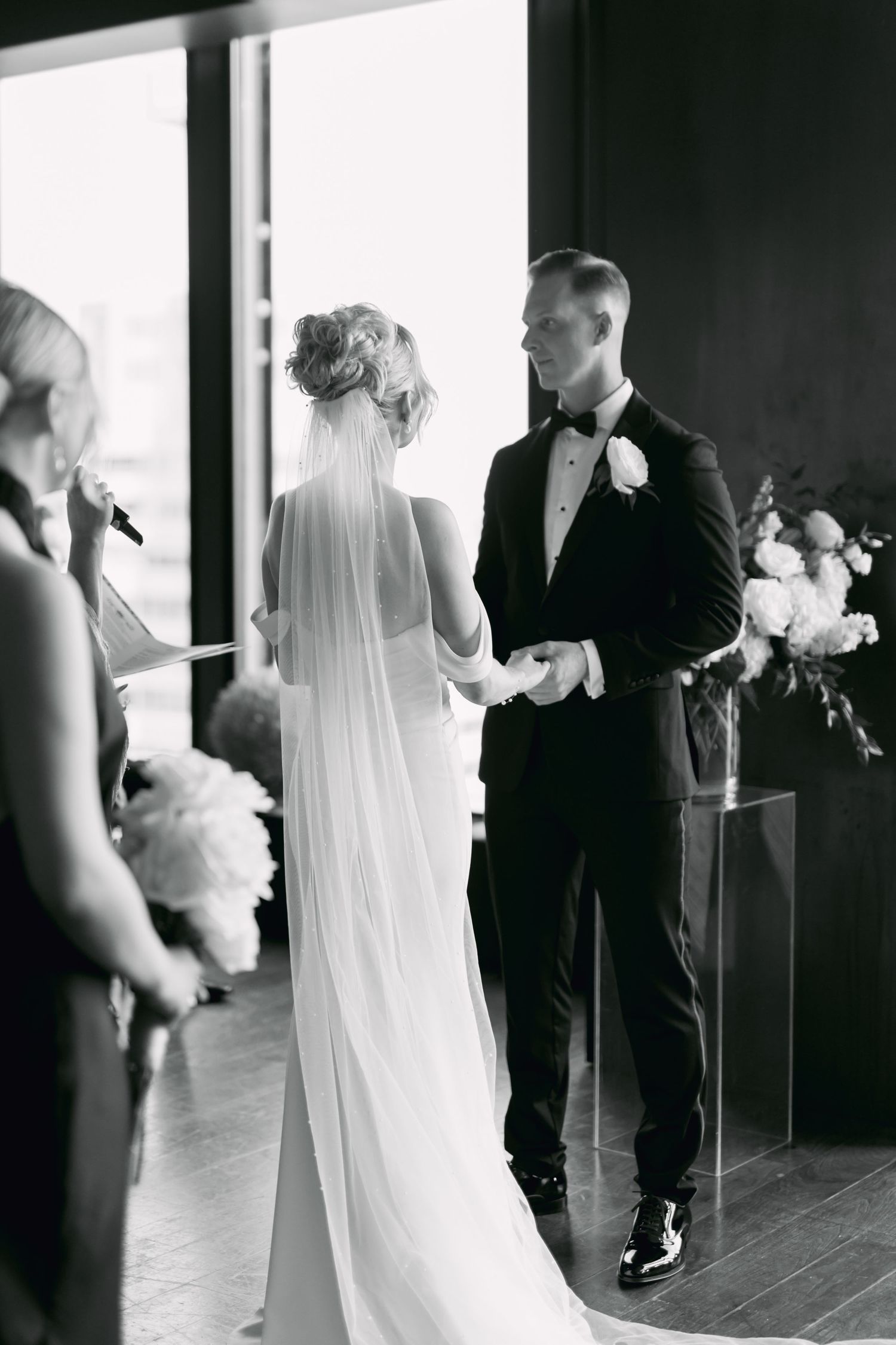 Black and white photo of bride and groom holding hands during intimate indoor wedding ceremony.