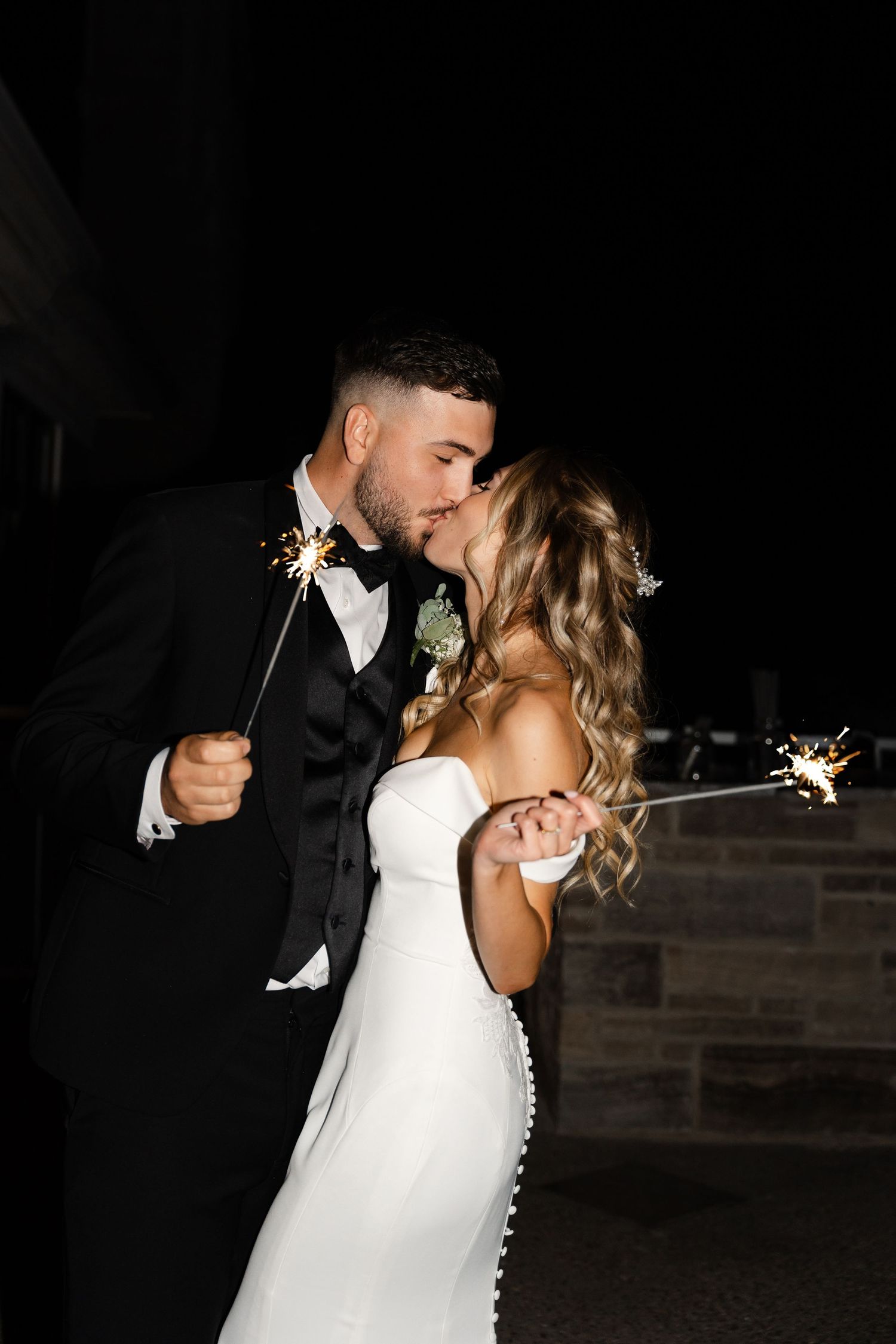 Couple celebrates with sparklers during nighttime wedding festivities.