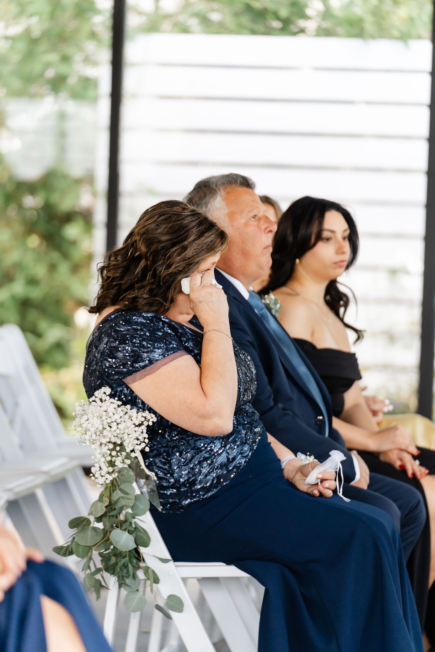 Wedding guests in formal navy attire showing emotional reactions during ceremony.