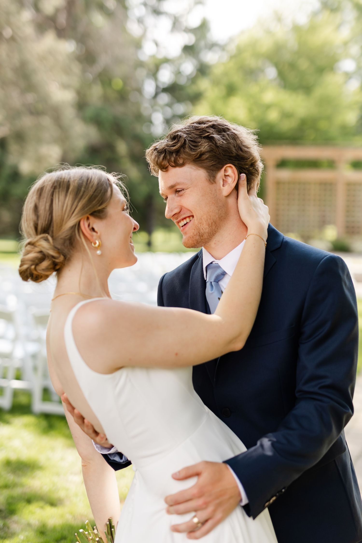 Romantic wedding couple embracing outdoors in formal attire on sunny day.