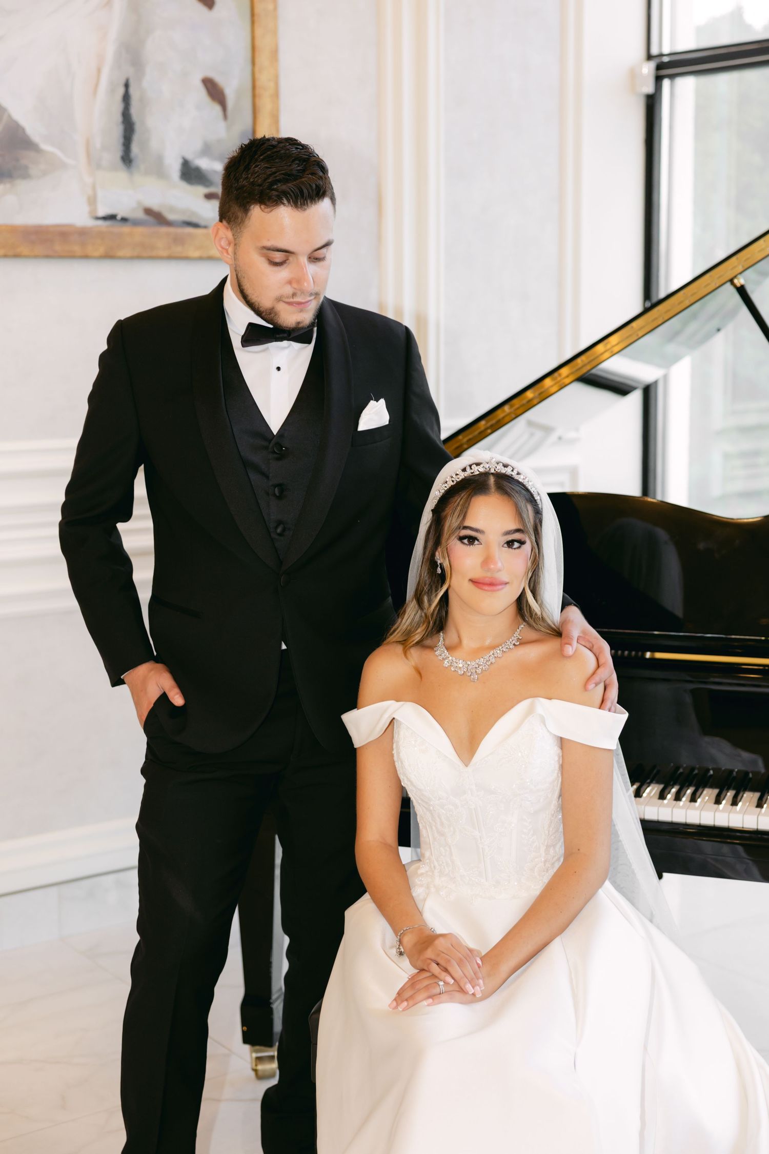 Elegant wedding couple poses in bright indoor venue with grand piano.