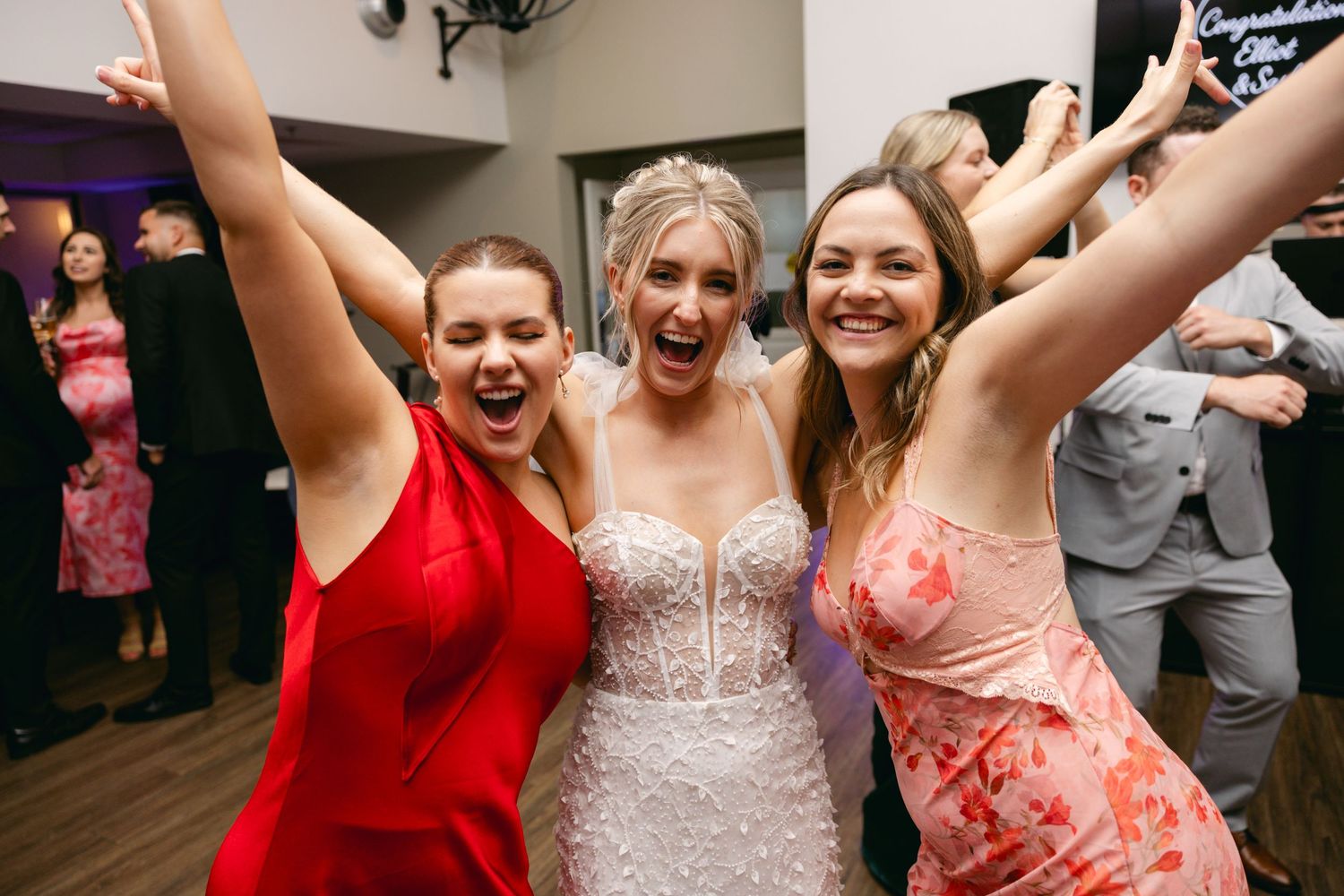 Energetic dance party with guests and wedding party members raising hands in celebration.