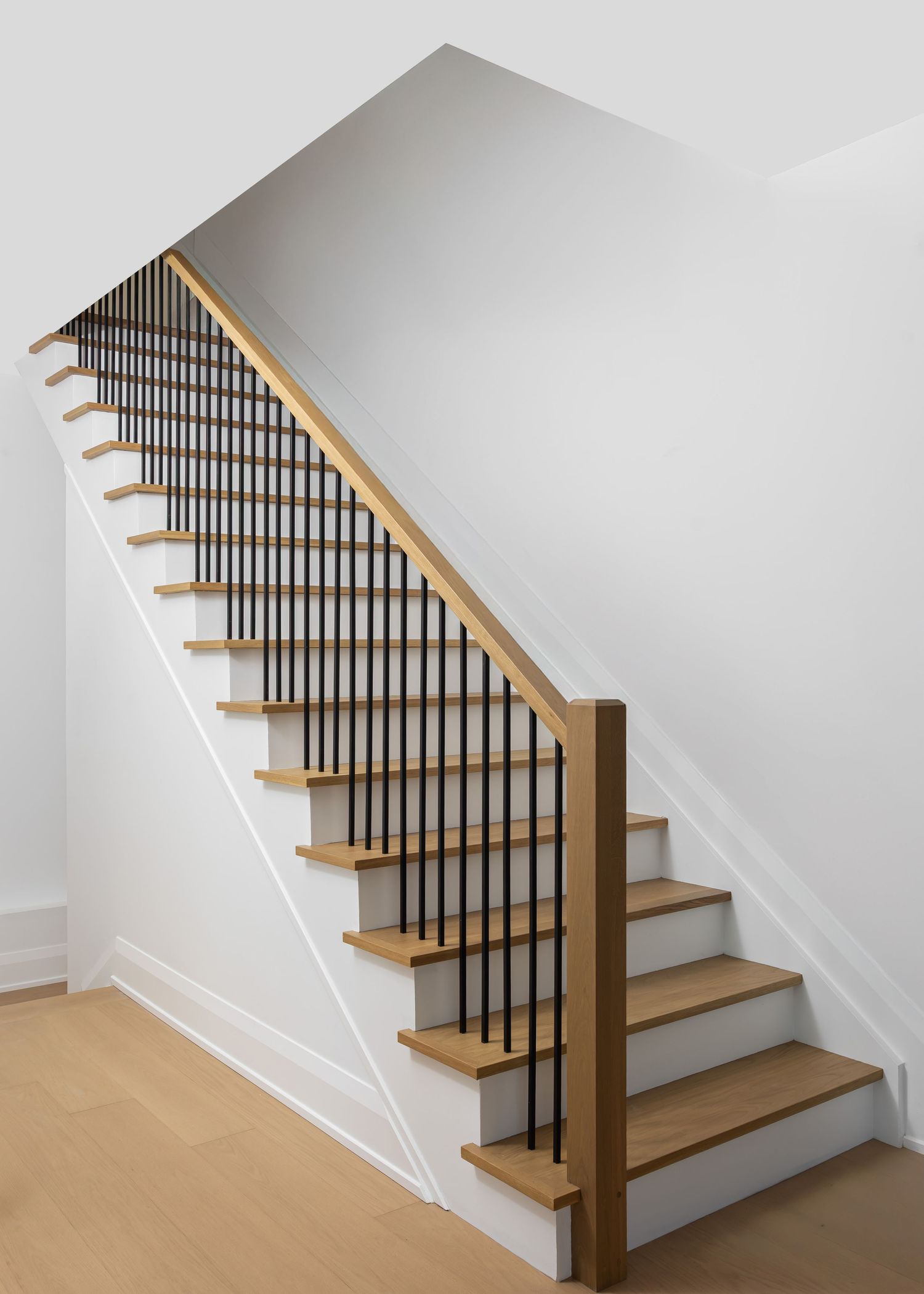 Contemporary staircase with black metal spindles, wooden treads, and white walls in a minimalist design.