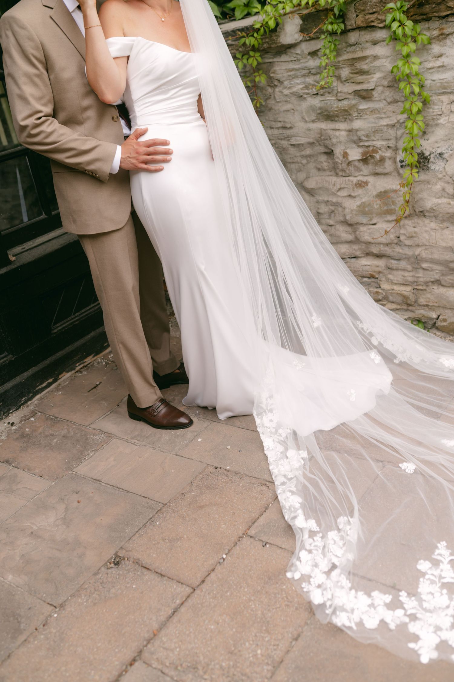 Elegant bridal veil with lace trim details flows across stone courtyard.
