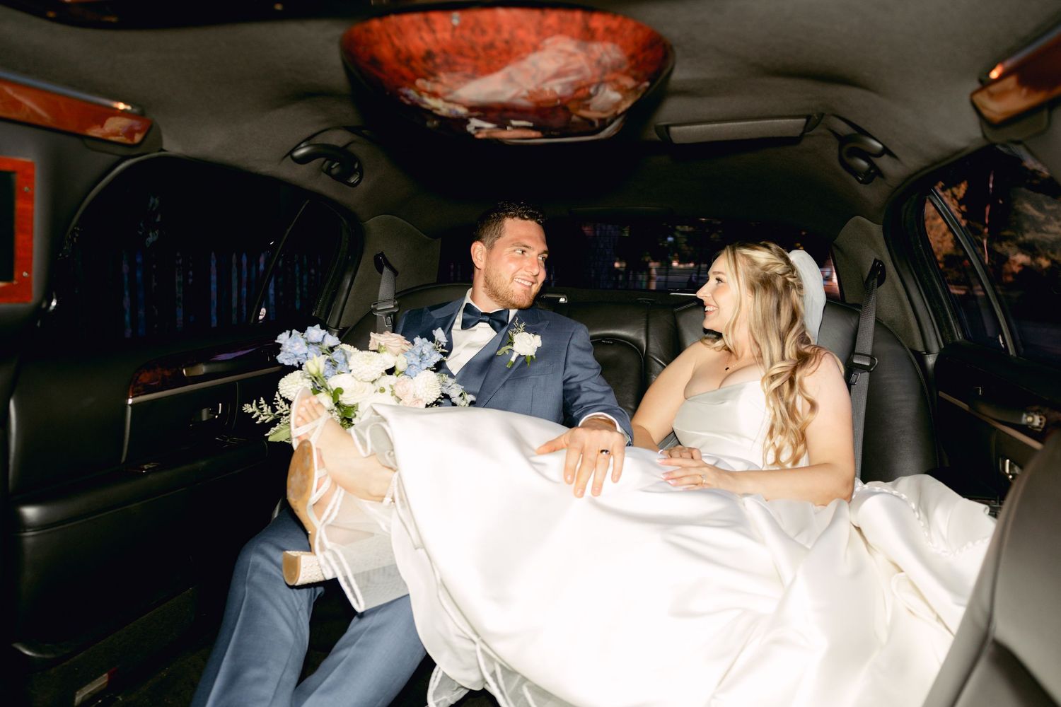 Wedding couple sharing champagne together in the back of a car during their celebration.