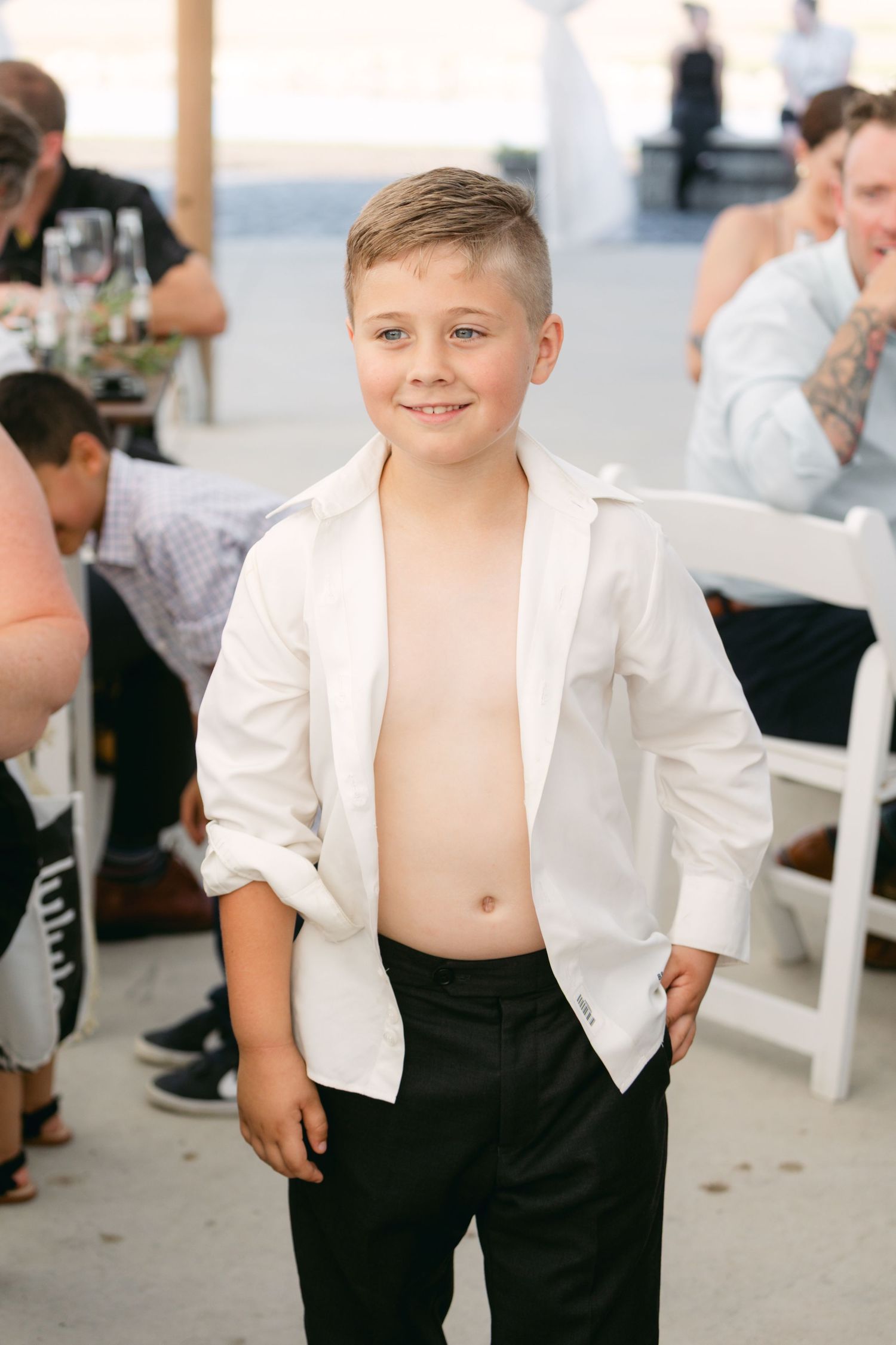 Young ring bearer in formal attire poses at outdoor wedding reception.
