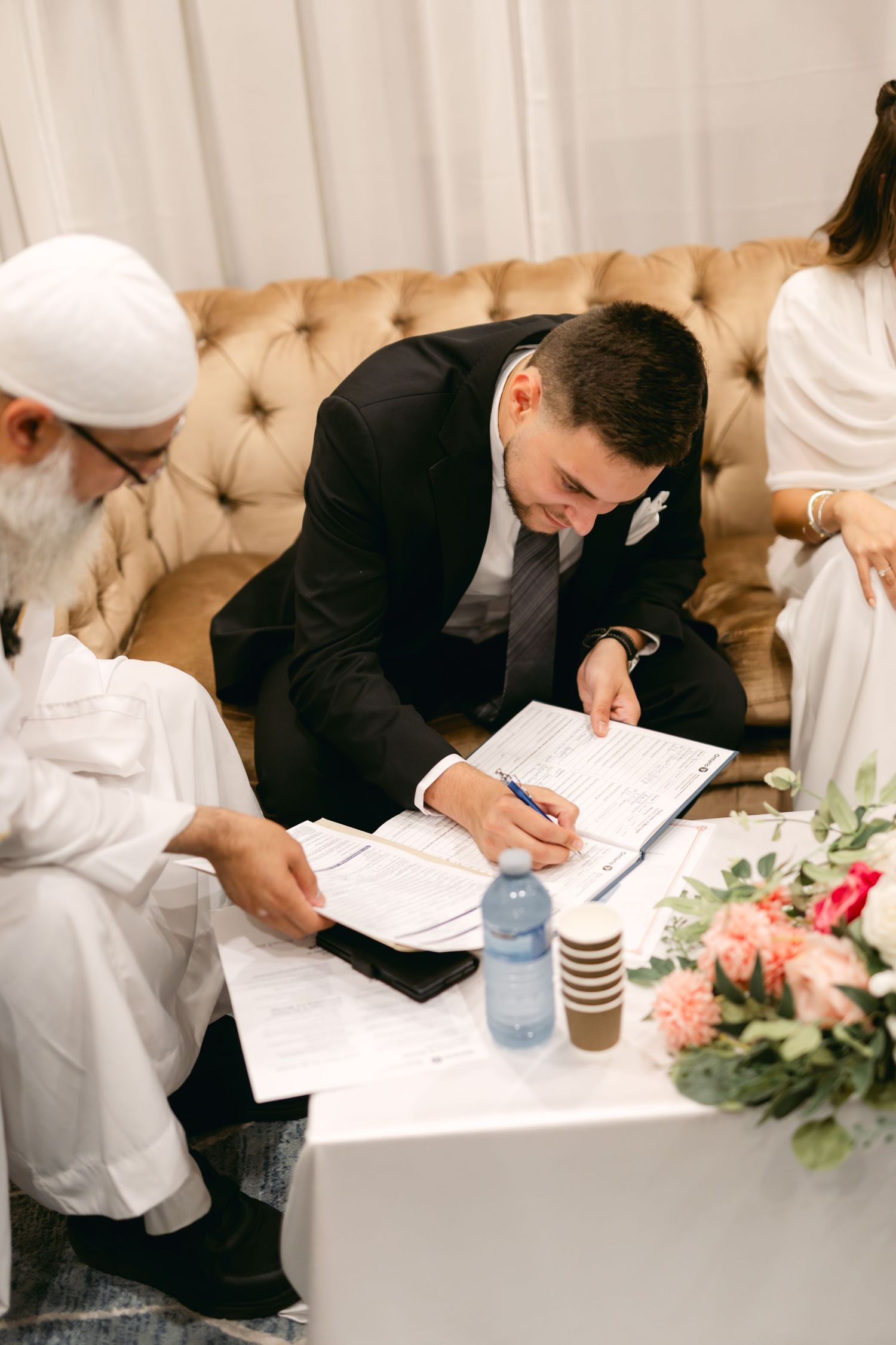 A person signs documents on a coffee table during a formal ceremony with floral decorations.