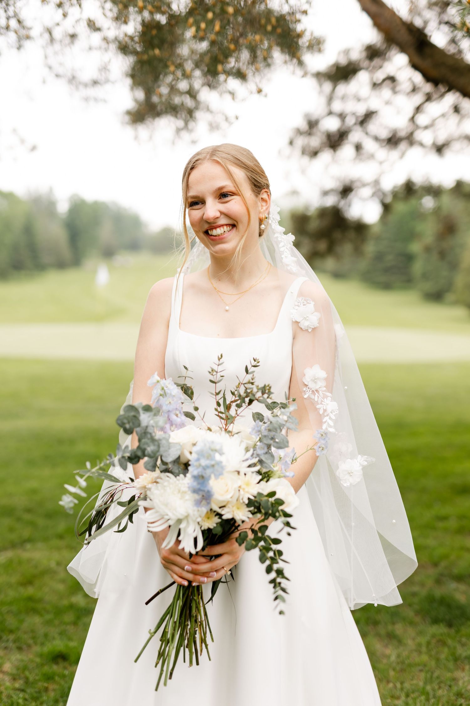 Bride in classic white gown holds stunning bouquet of white flowers and greenery.