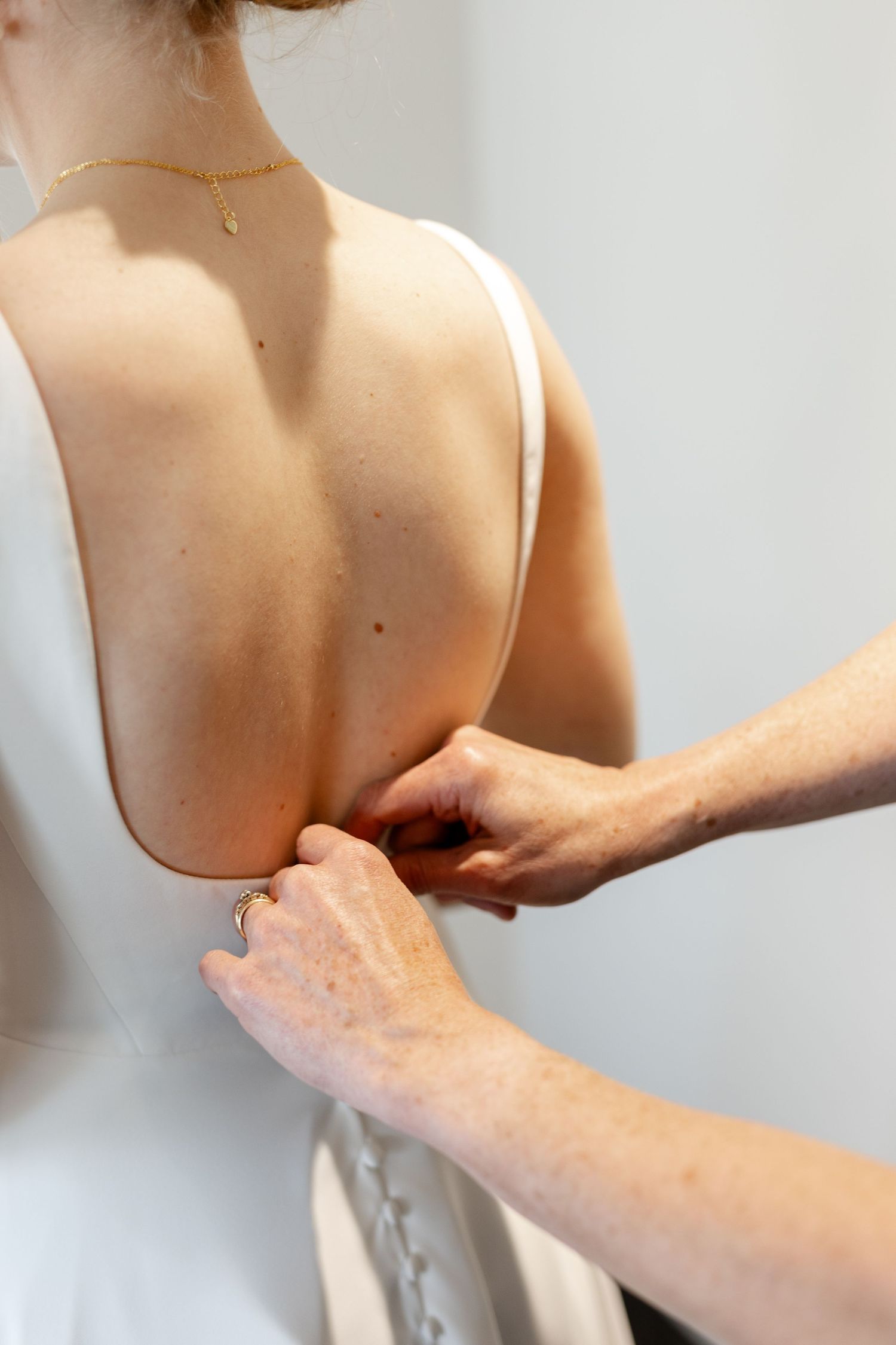 Close-up of hands adjusting the back of a white wedding dress.