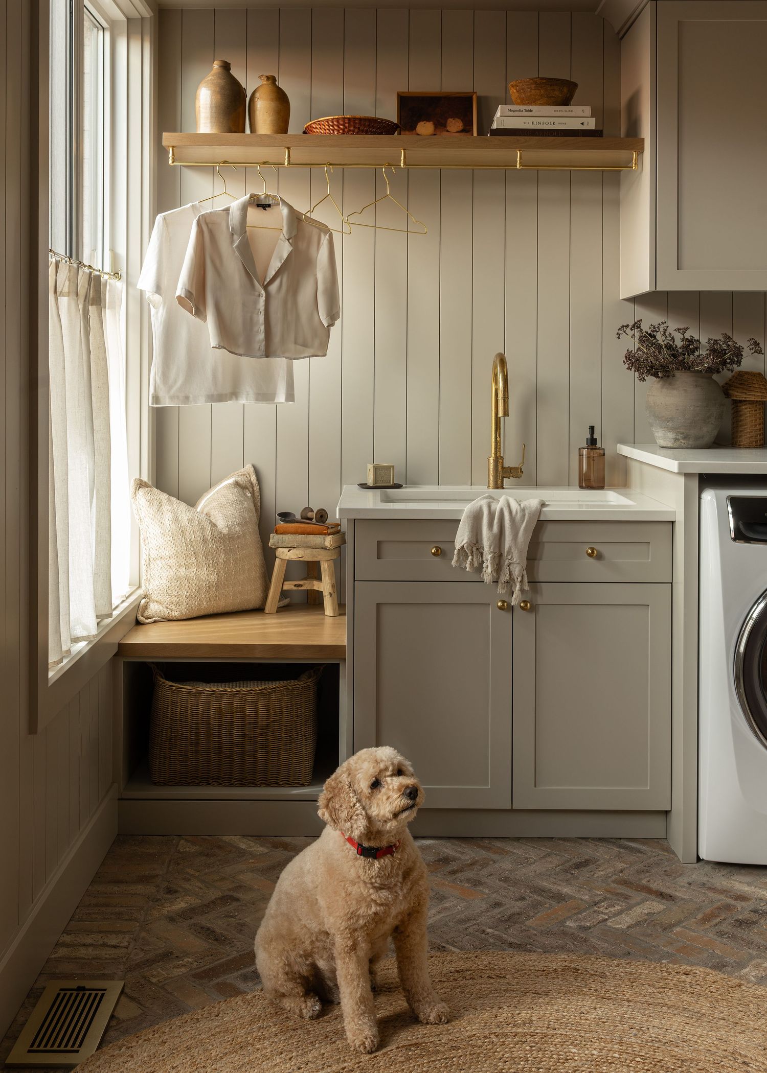 Cozy laundry room featuring gray cabinets, wooden shelves, and a fluffy dog on herringbone flooring.