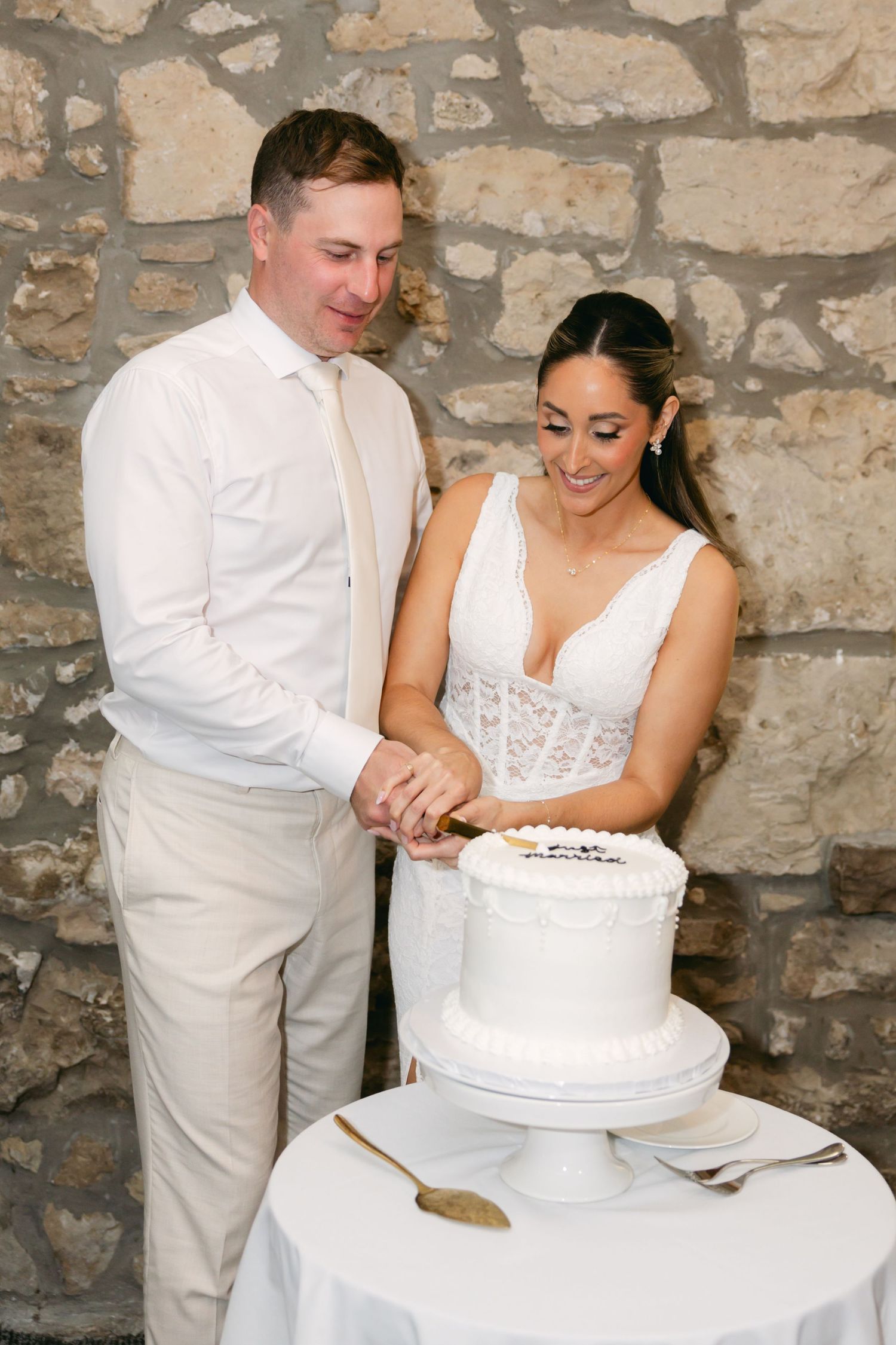 Wedding couple cutting their white wedding cake together in stone venue.