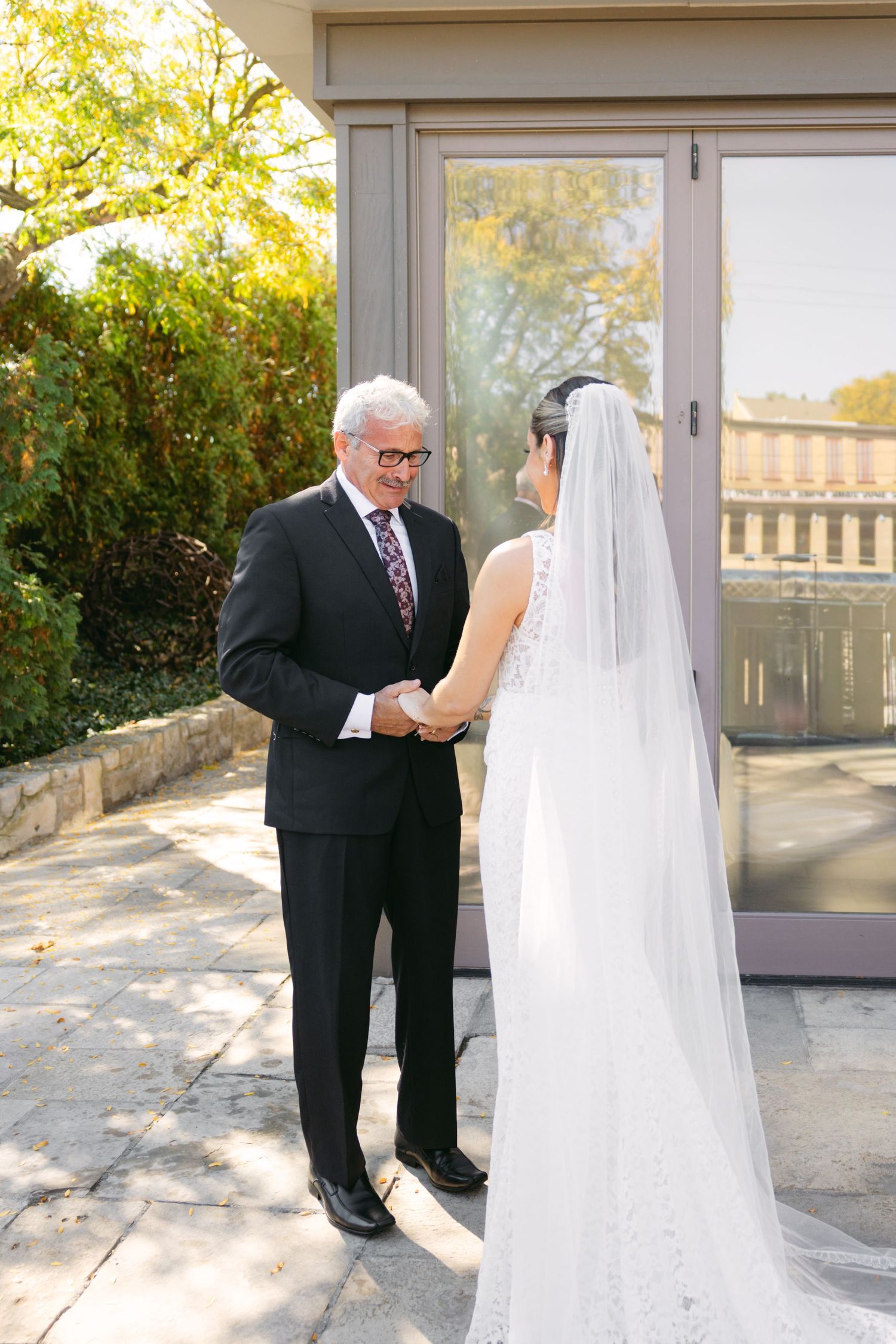 An officiant in glasses and dark suit reads from papers while speaking to a bride in her wedding gown.