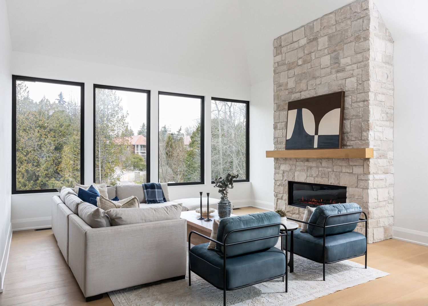 Contemporary living room with stone fireplace, large windows, and blue accent chairs.