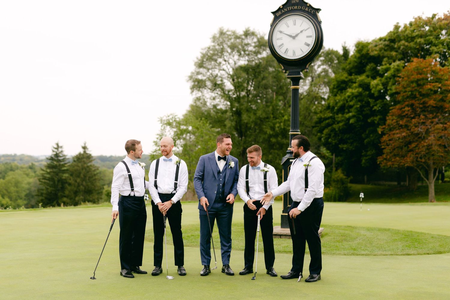 Groomsmen lined up on golf course with decorative clock and trees in background.