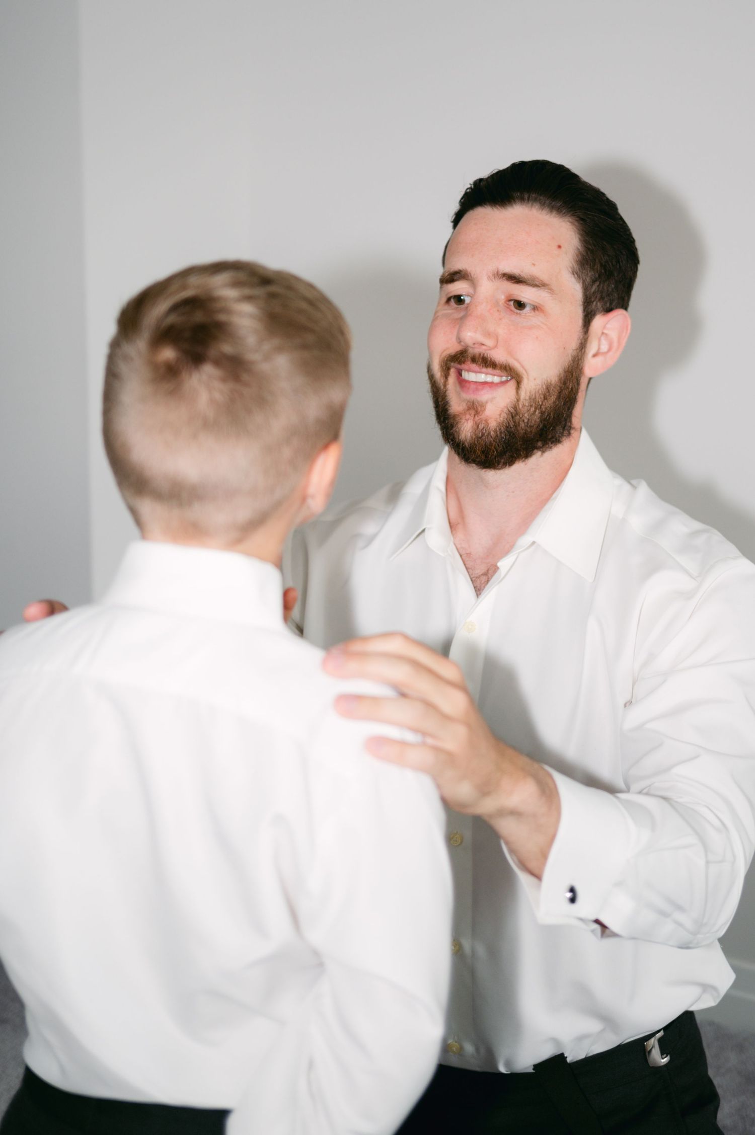 Two people in white dress shirts share a lighthearted moment against a plain background.