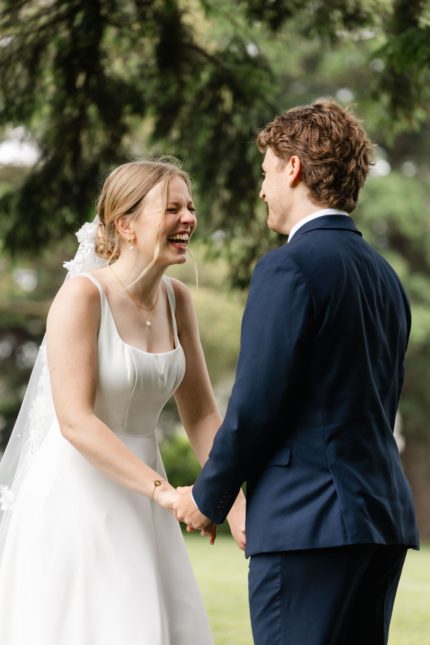 A joyful wedding moment captured as the couple shares laughter under pine trees.