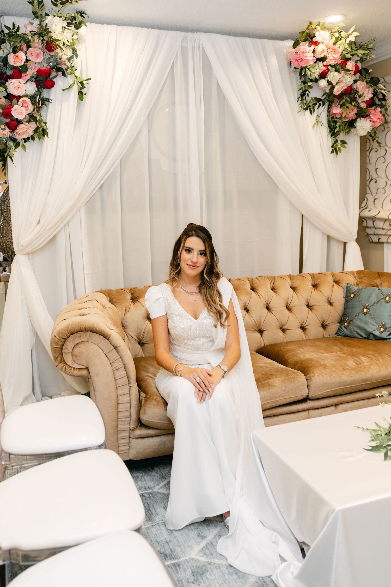 Elegant bridal setting with tufted beige couch and floral arrangements.