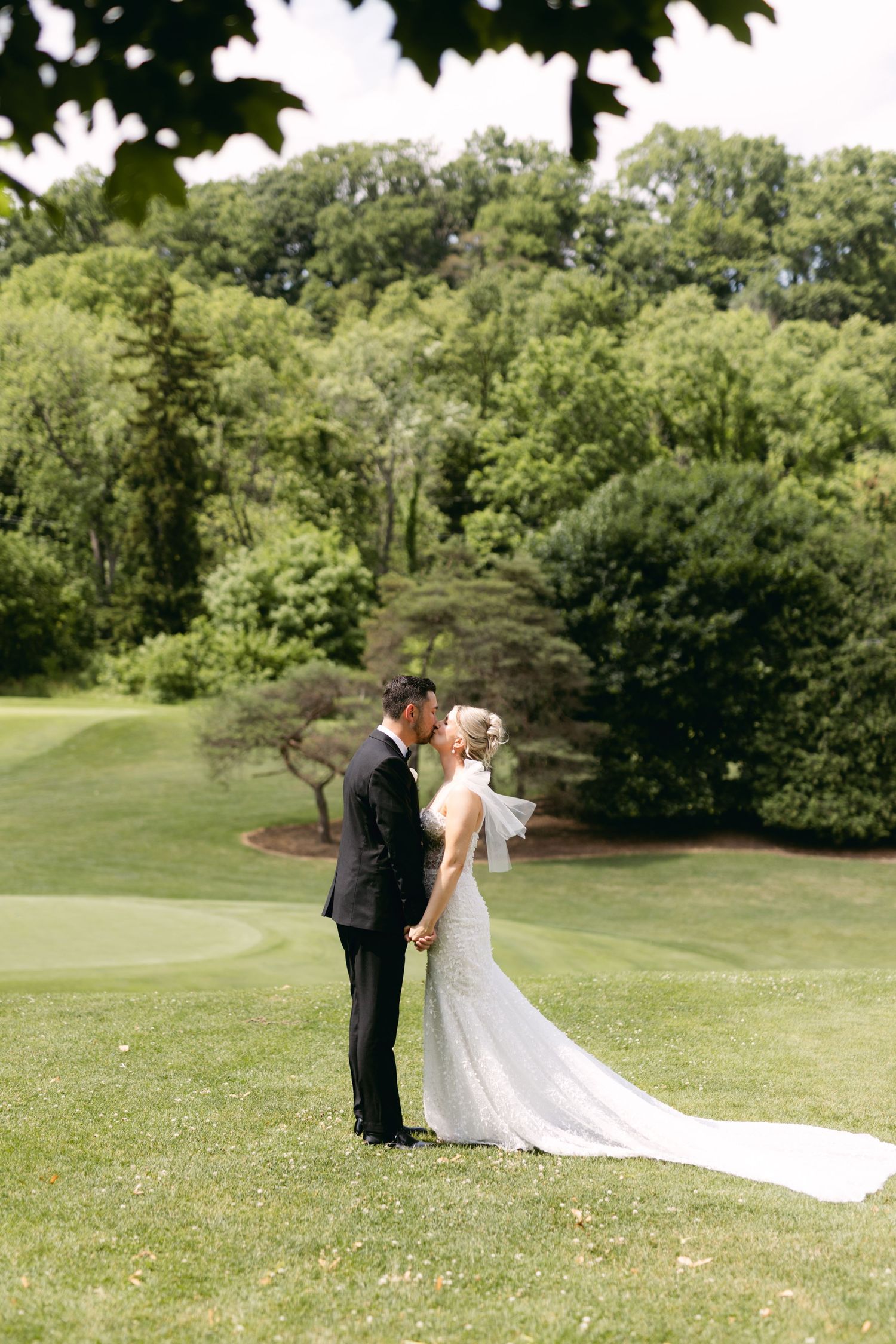 A wedding couple standing on a golf course hill surrounded by lush green trees.
