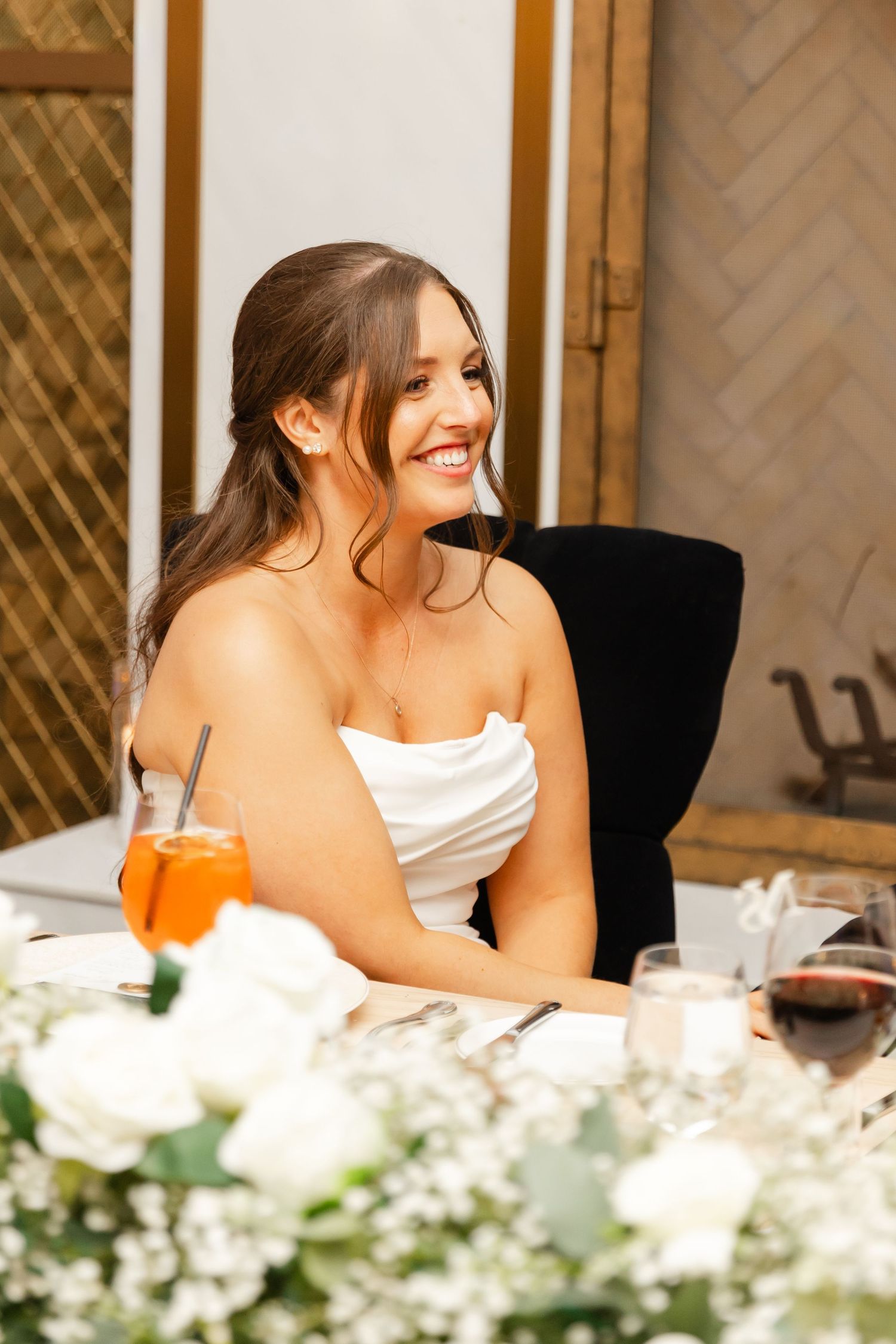 Radiant bride in strapless white gown smiles joyfully while seated at the wedding reception table.
