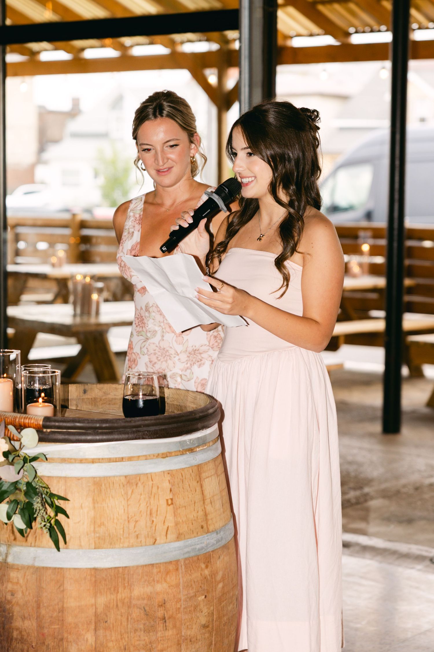 Bridesmaids in light pink dresses share laughs around rustic barrel decor.