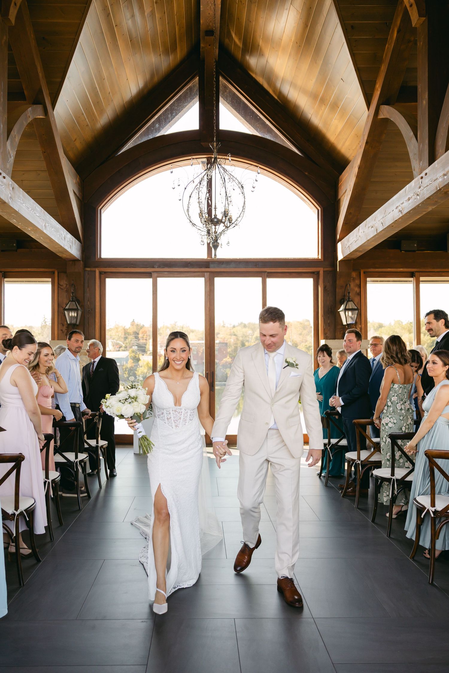 Wedding celebration in bright rustic venue with exposed beams and large arched windows.