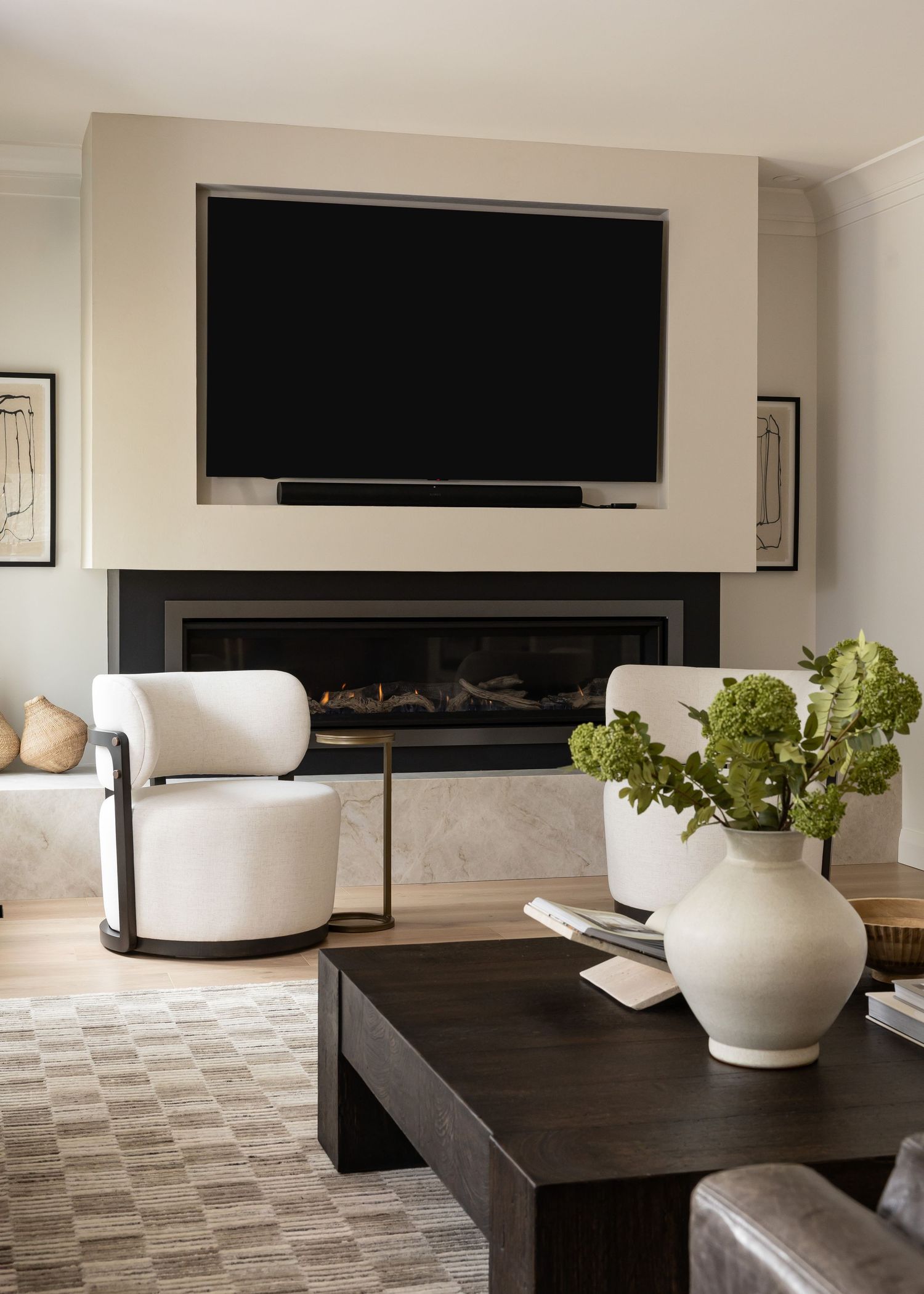 Elegant living area with white chairs, dark coffee table, and decorative plants near a linear fireplace.