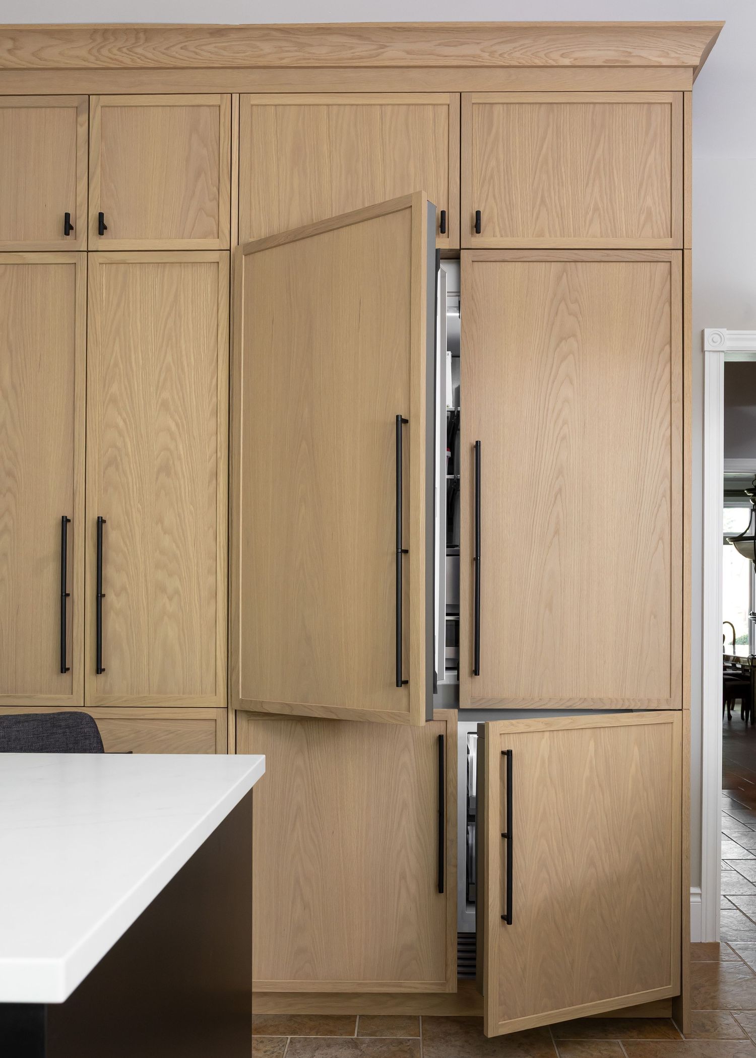 Floor-to-ceiling wood cabinet storage with black handles and white countertop peninsula.