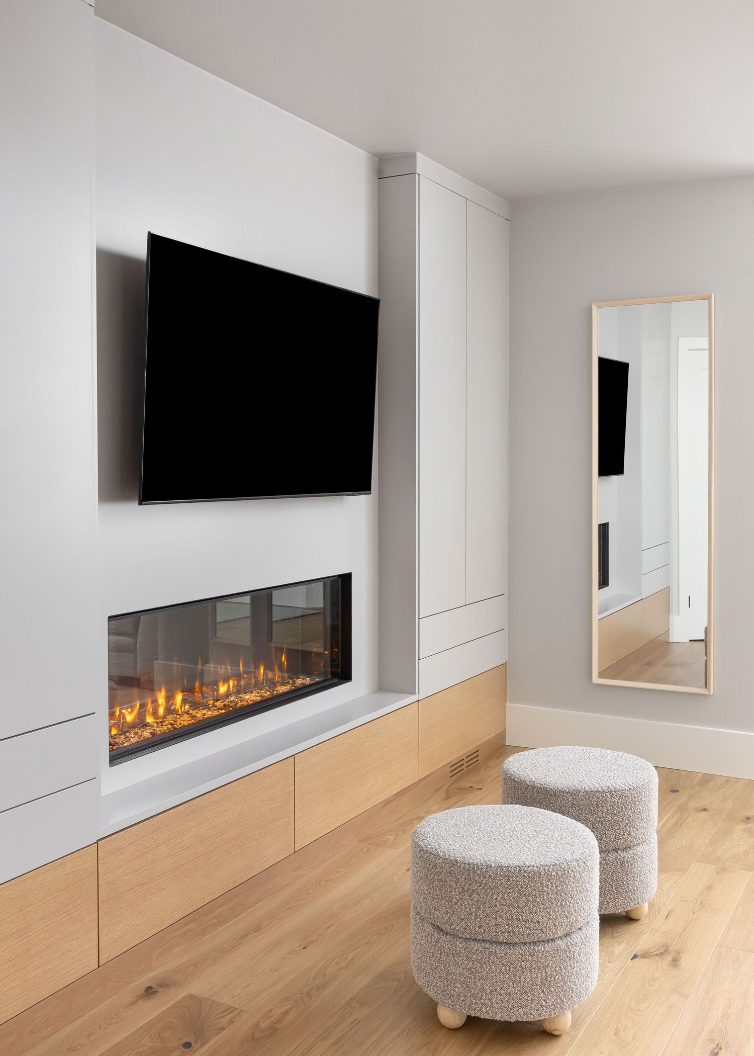Modern living space with built-in electric fireplace, wall-mounted TV, and textured ottoman seating.