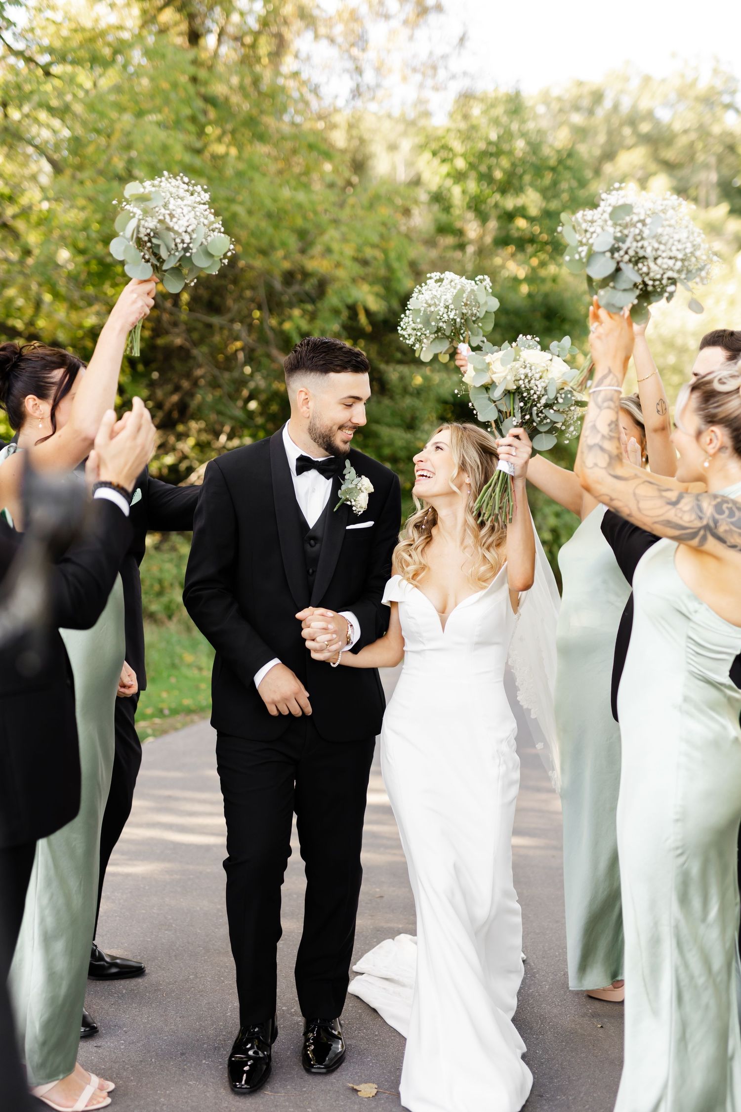 Wedding party celebrating with joyful poses in mint green dresses and black tuxedos.