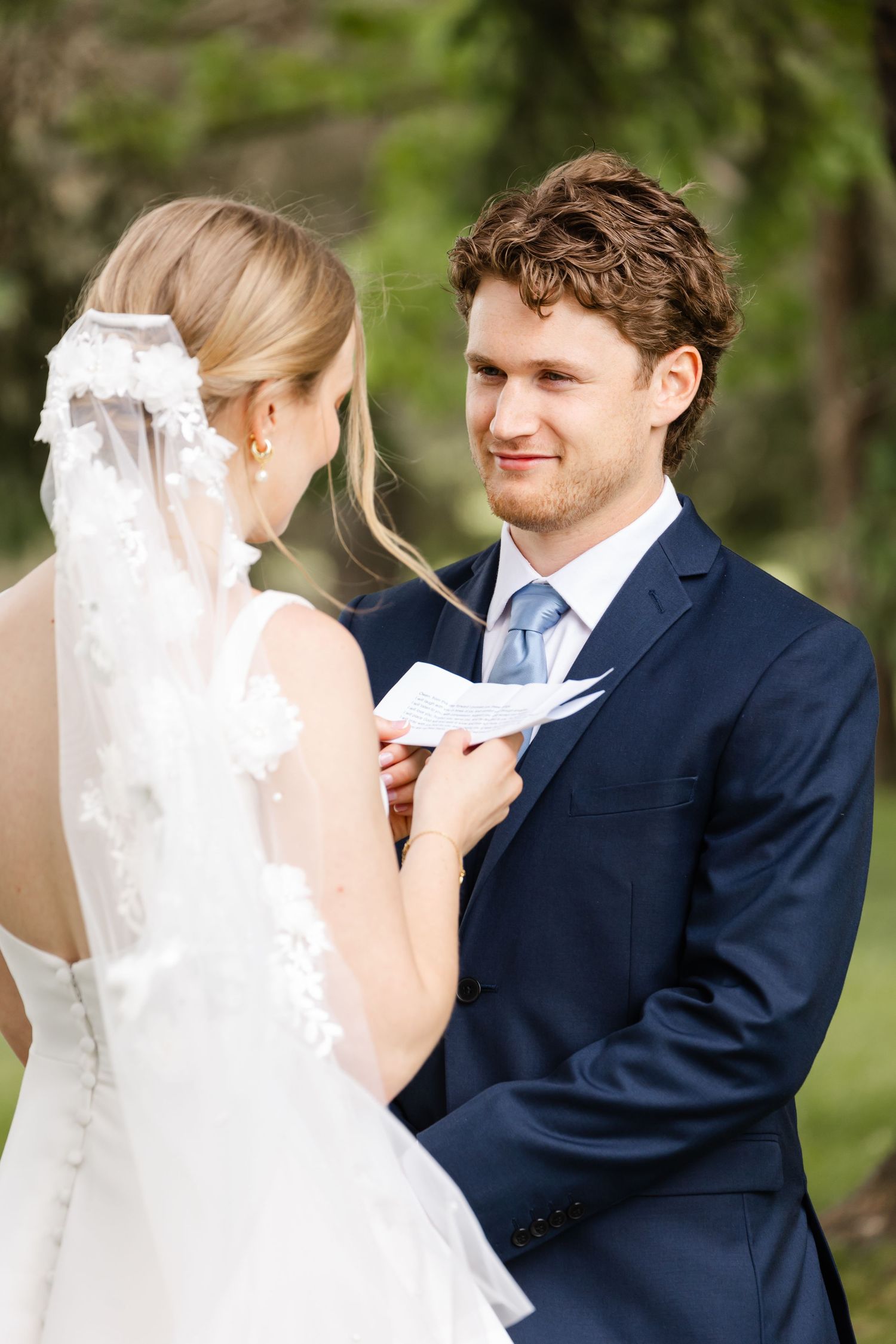 A tender moment between newlyweds as they exchange written vows in a garden setting.