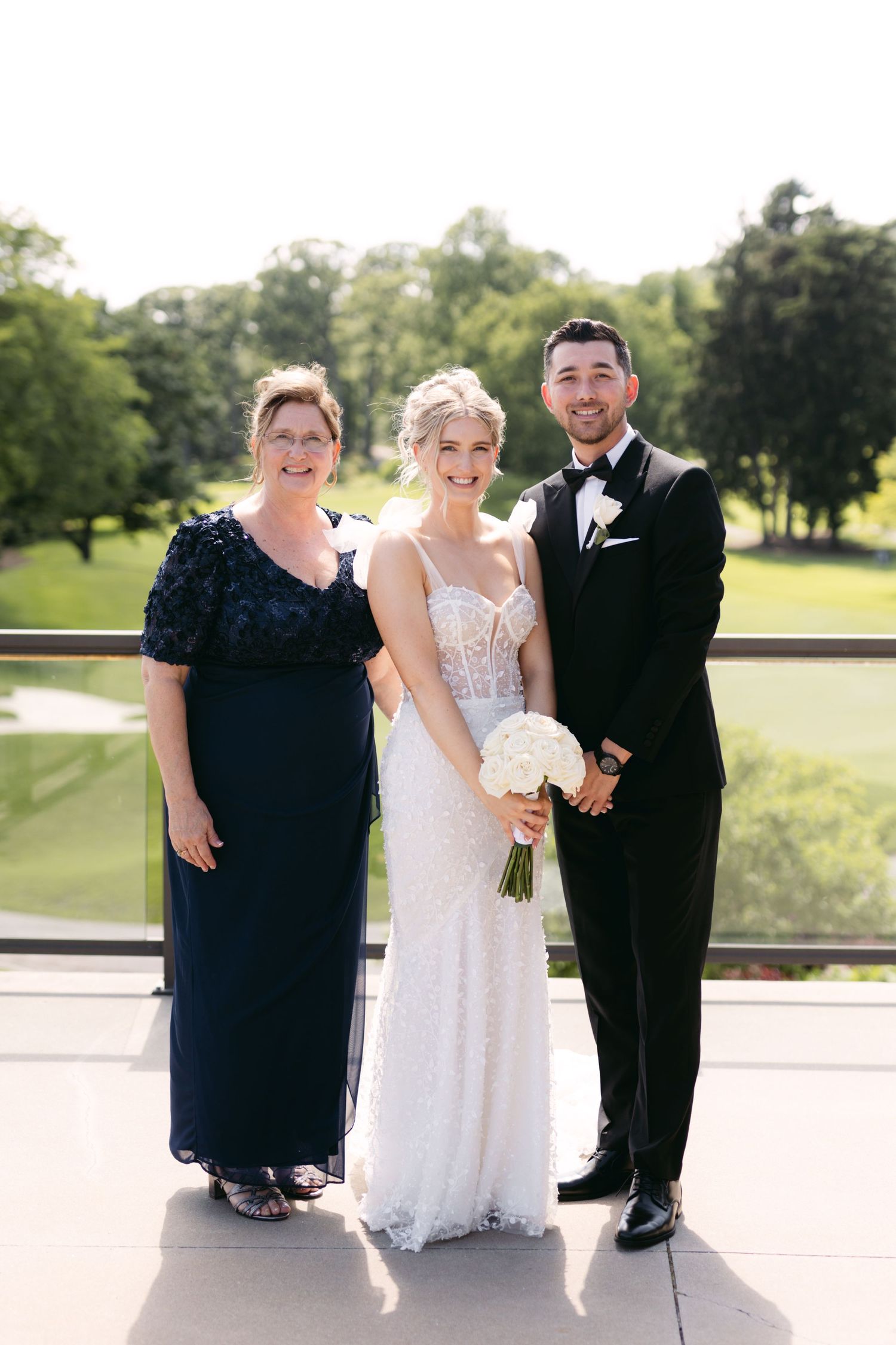 Small wedding party group poses casually on sunny outdoor venue patio.