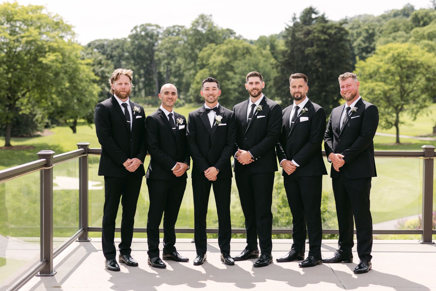 Groomsmen in matching black tuxedos pose together on an outdoor terrace.
