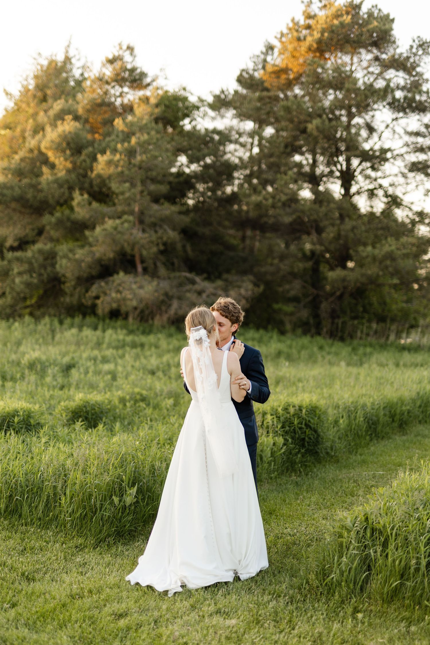 Bride and groom share romantic moments in a lush green field at golden hour.