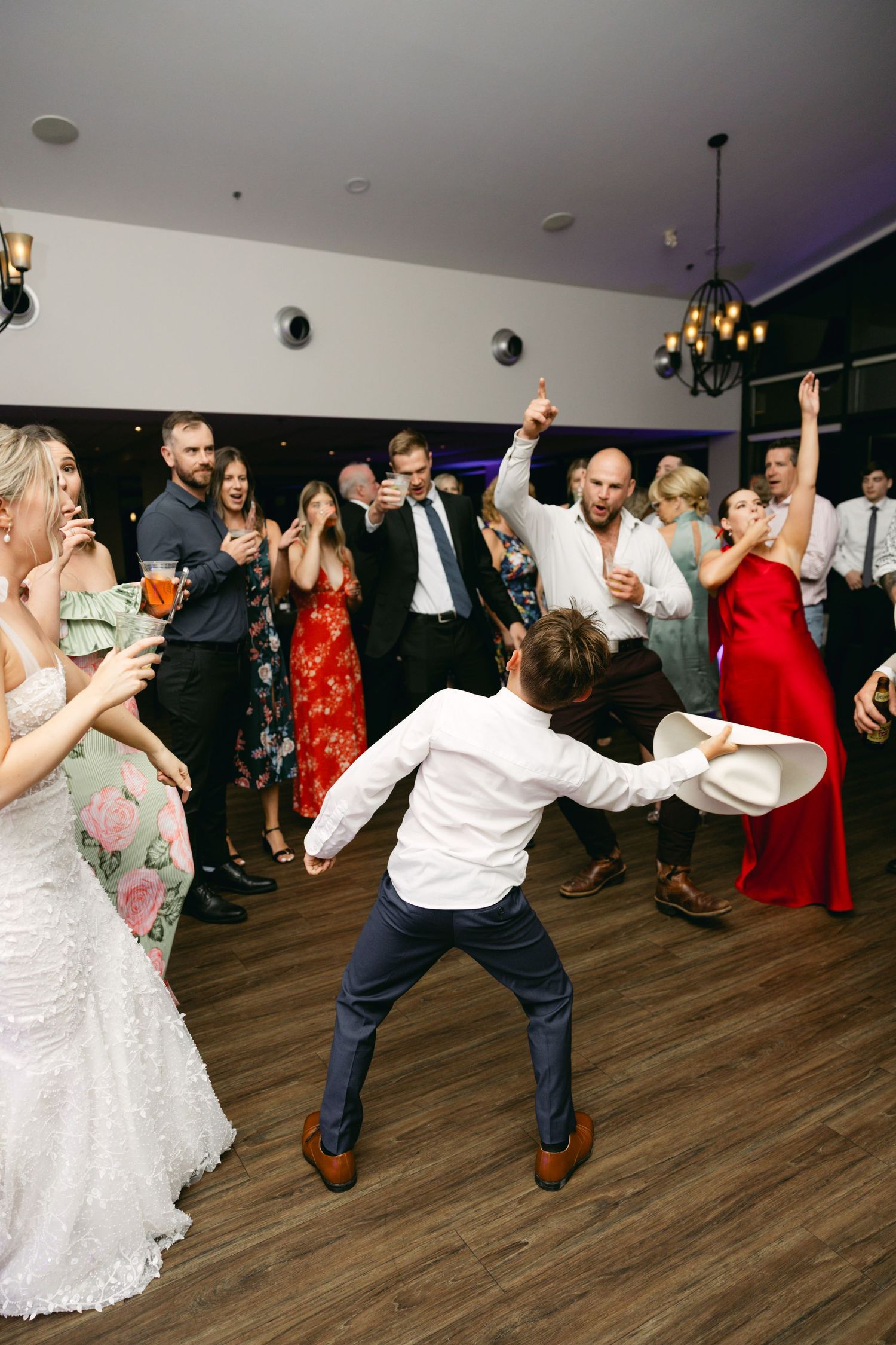 Wedding party members dance enthusiastically on wooden dance floor during reception.