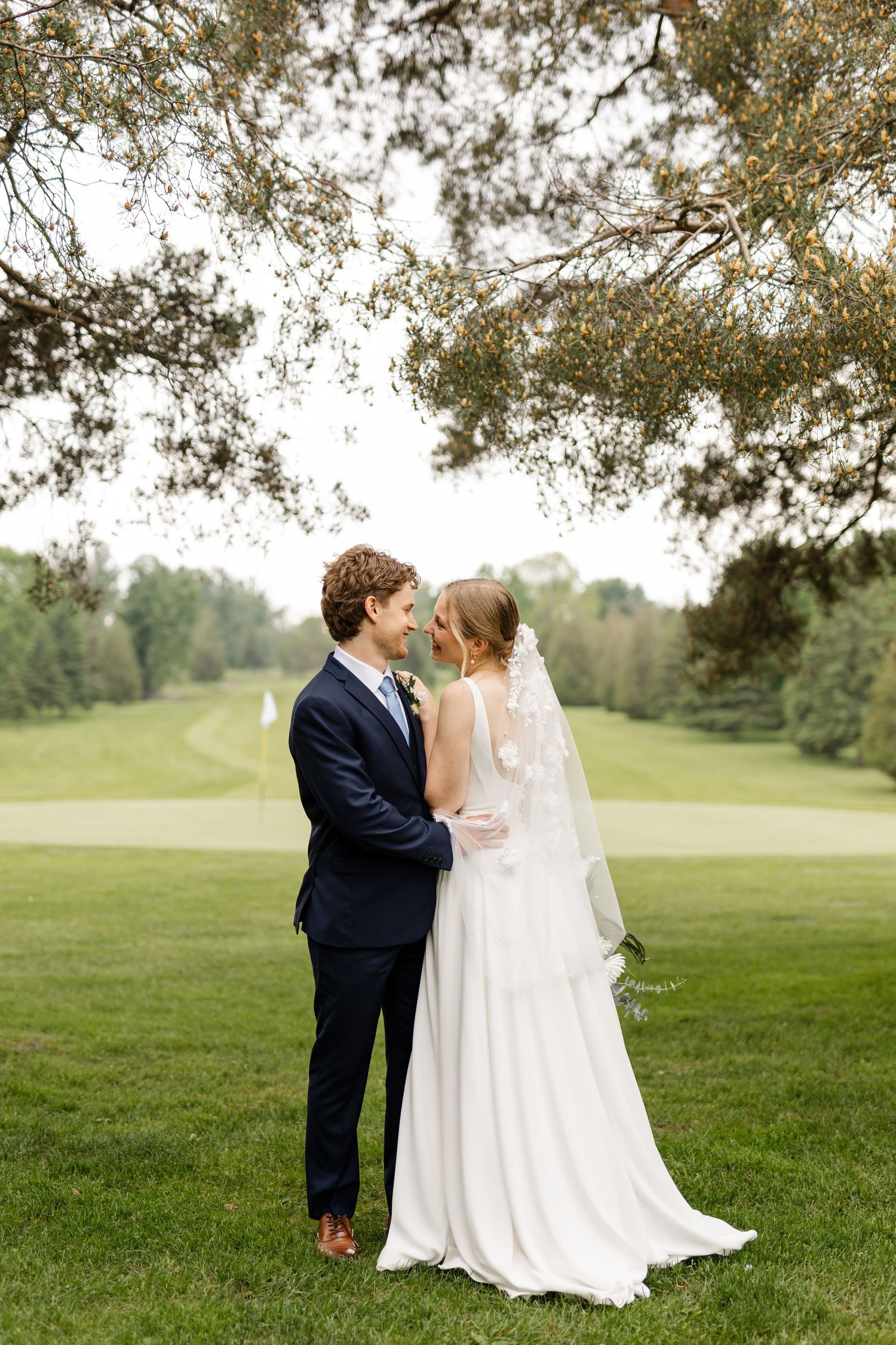 Romantic wedding portrait on golf course with pine trees in background.
