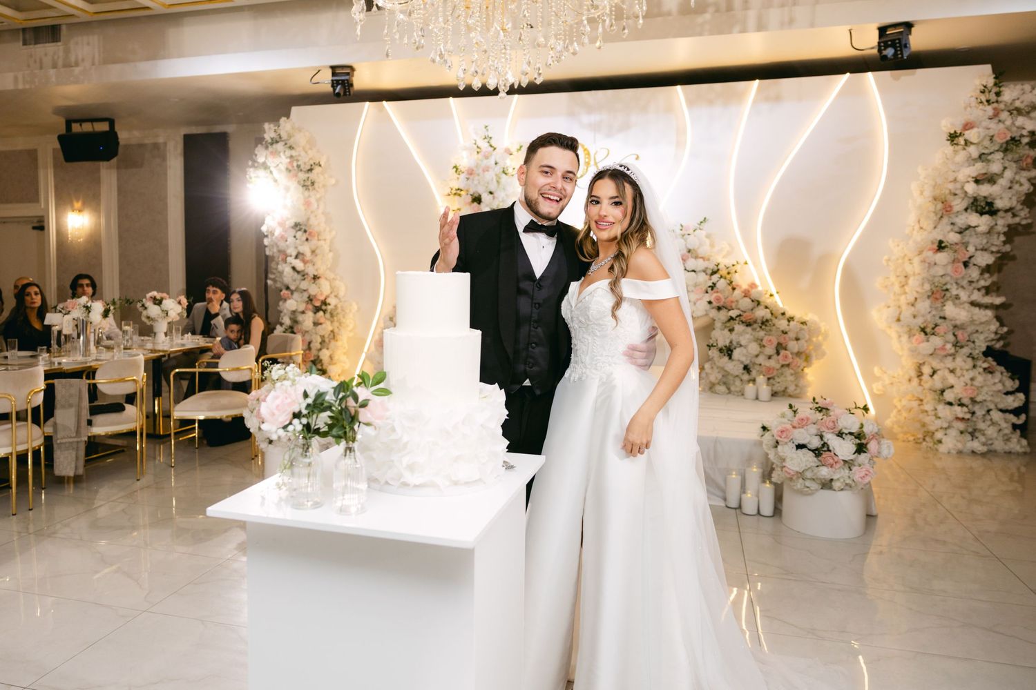 Wedding couple shares intimate moments in an elegant white venue with crystal chandeliers.