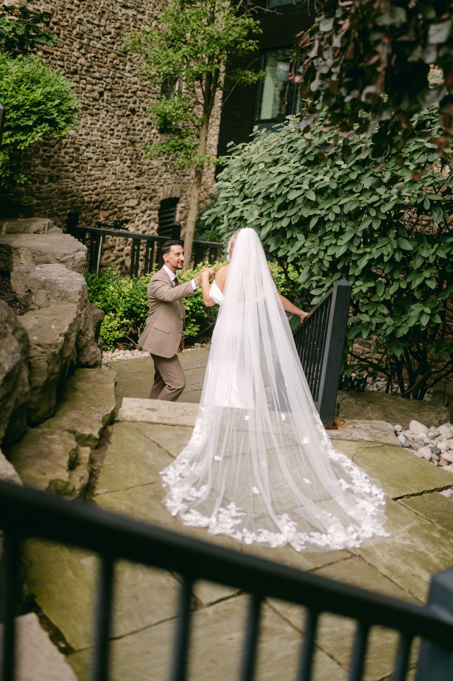 Beautiful cathedral veil with lace details trails behind bride in outdoor garden setting.