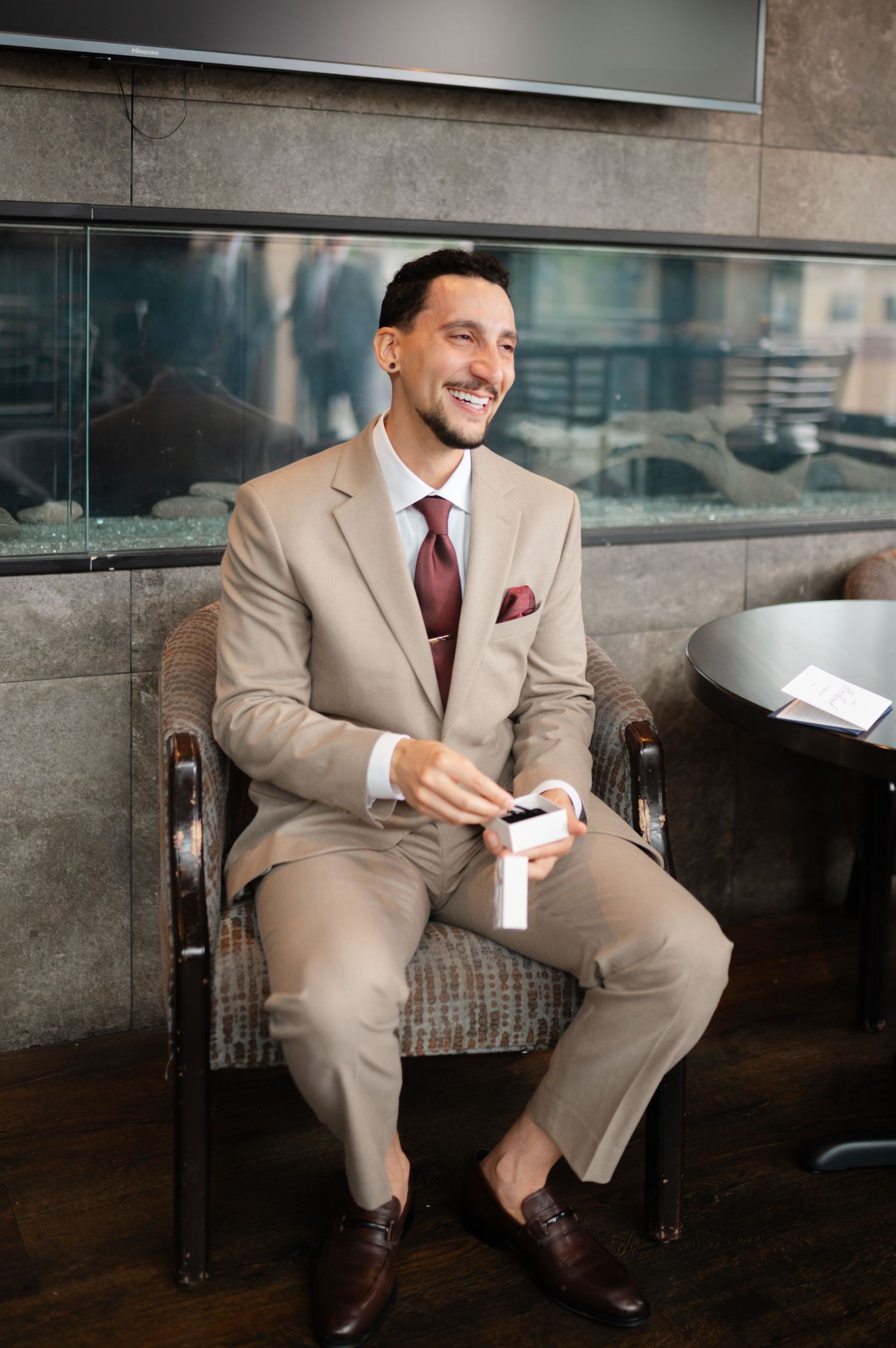 Businessman in tan suit smiles while seated in modern office setting.