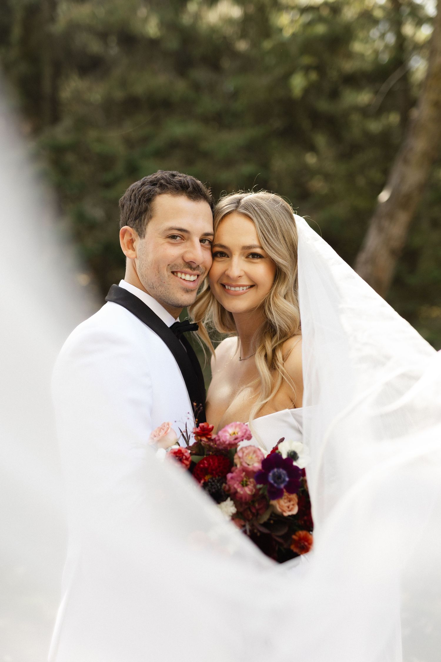 Romantic wedding portrait through flowing white veil with red bouquet.