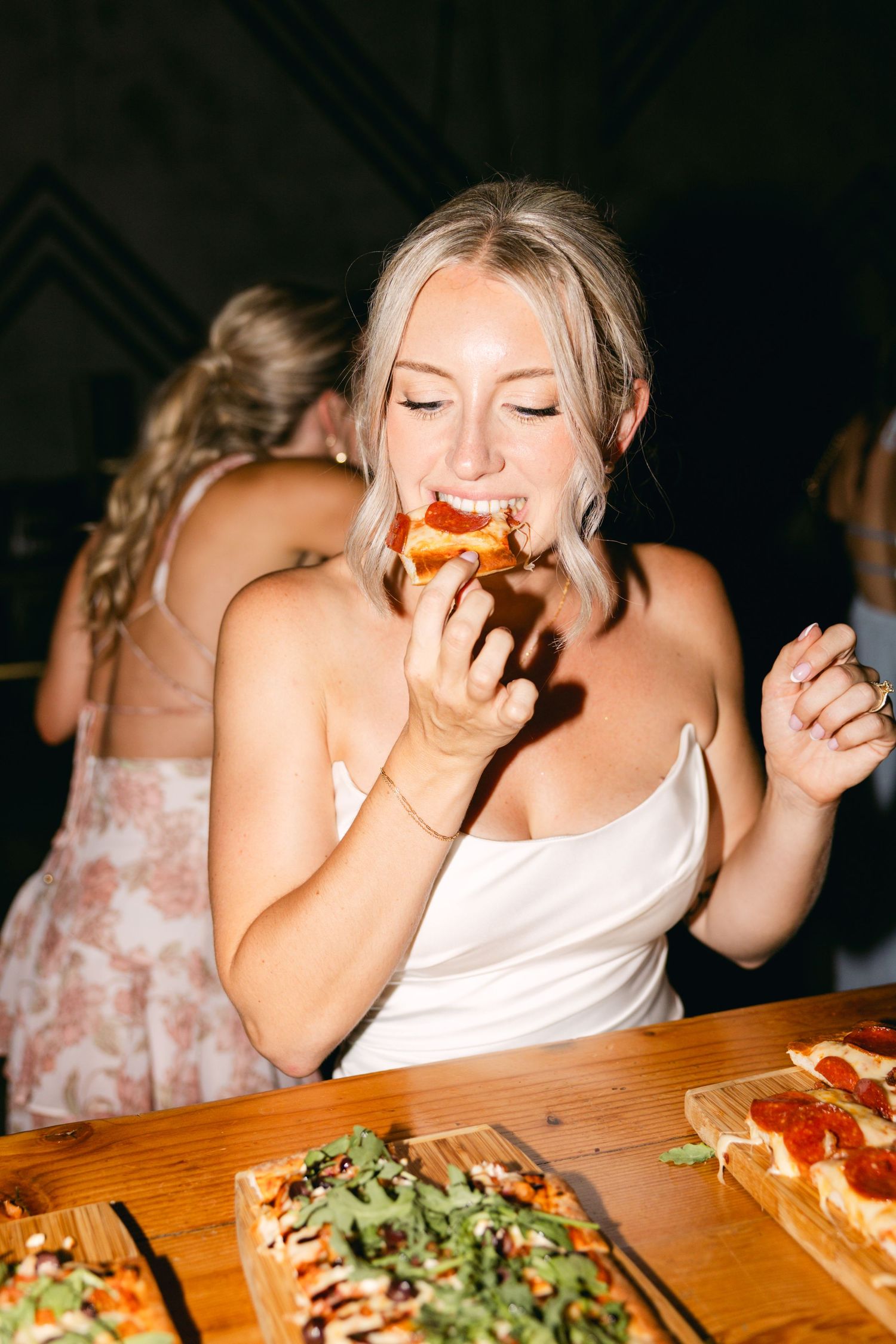 Wedding guest enjoying pizza at reception dinner under ambient lighting.