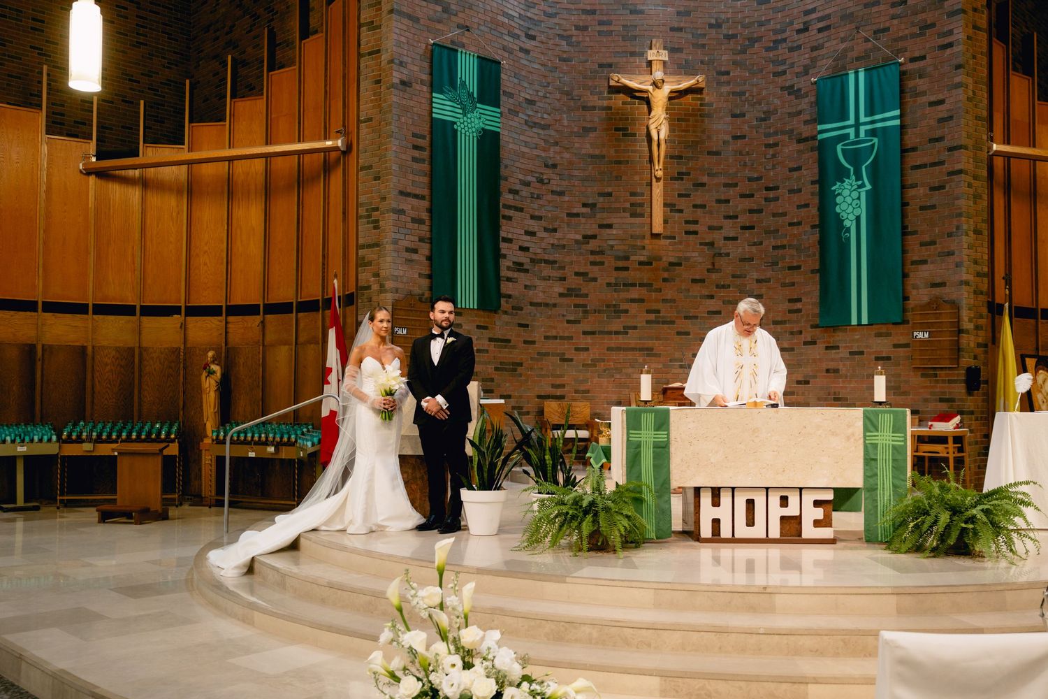 Bride and groom standing at church altar with priest during Catholic wedding ceremony.