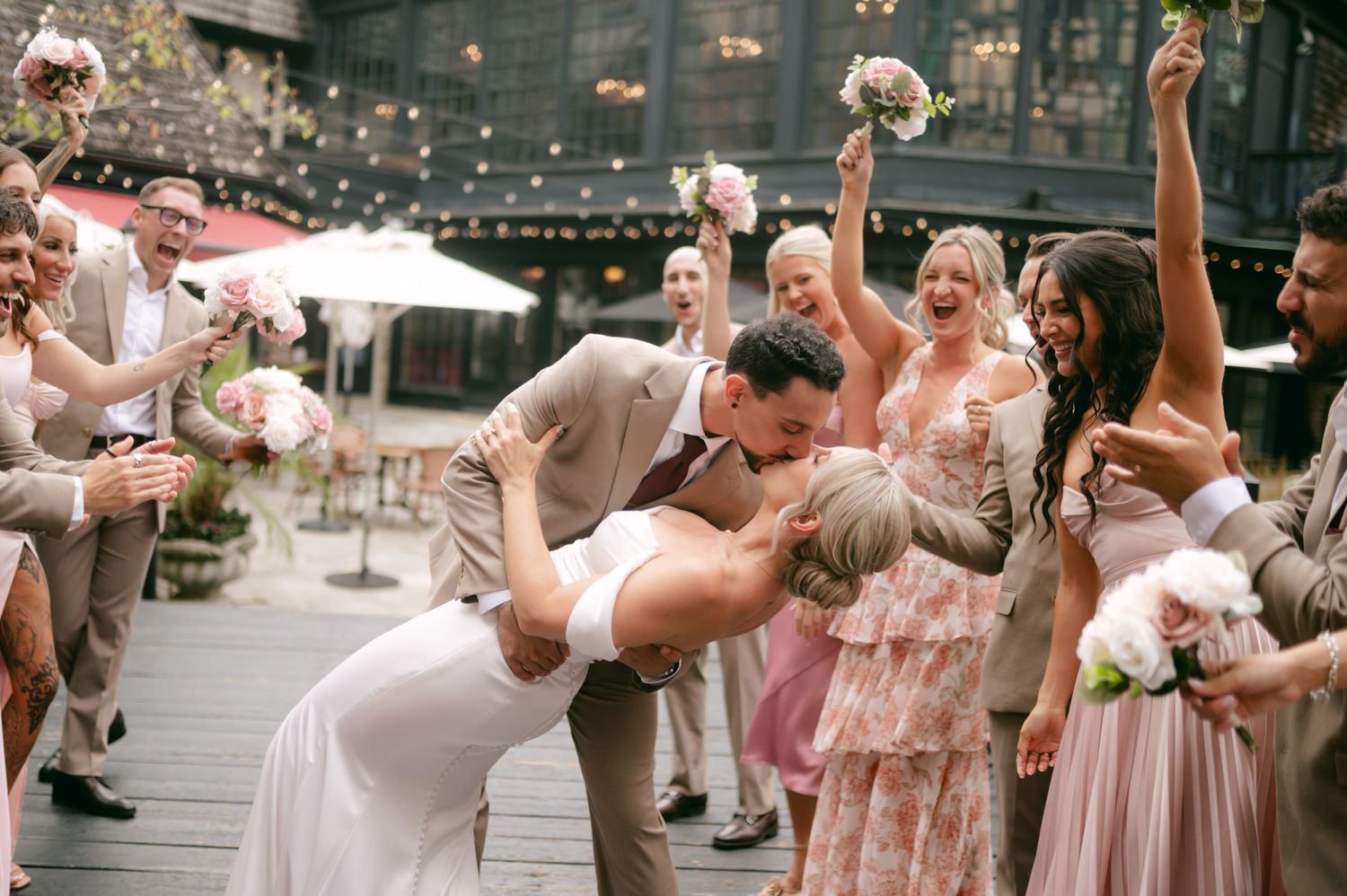 Wedding party celebrating with raised arms on an outdoor patio.