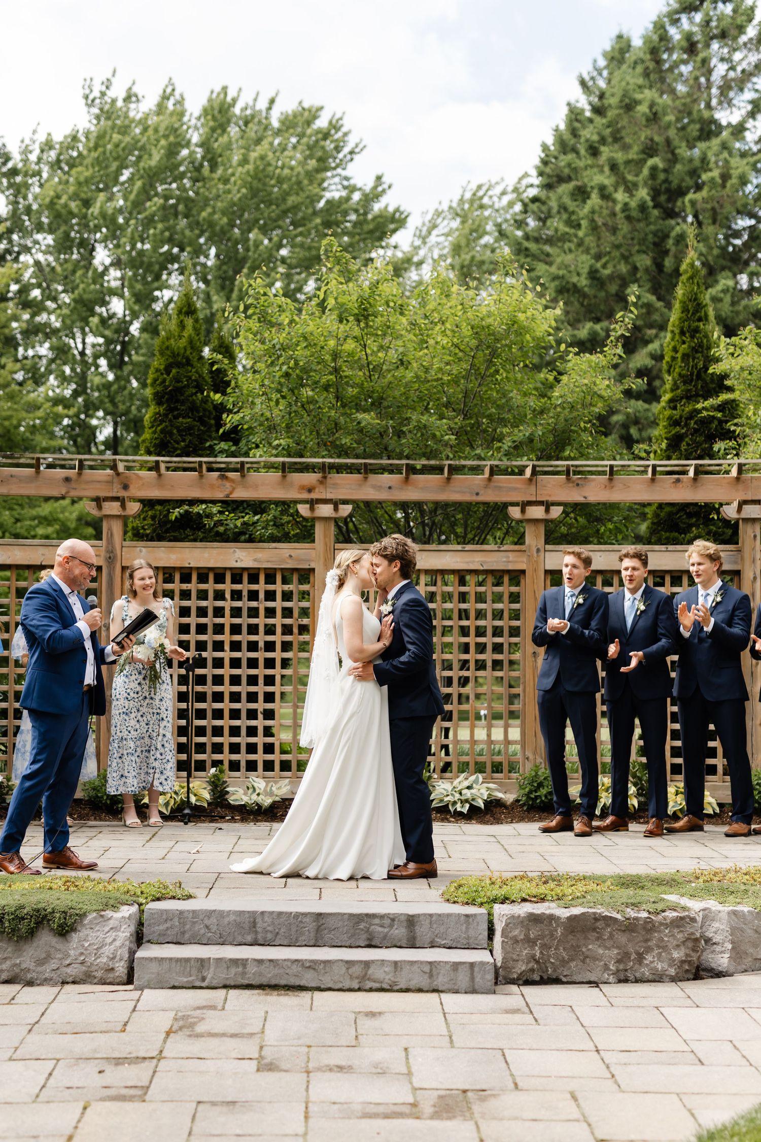 Wedding ceremony on stone platform with wooden lattice backdrop and wedding party in attendance.