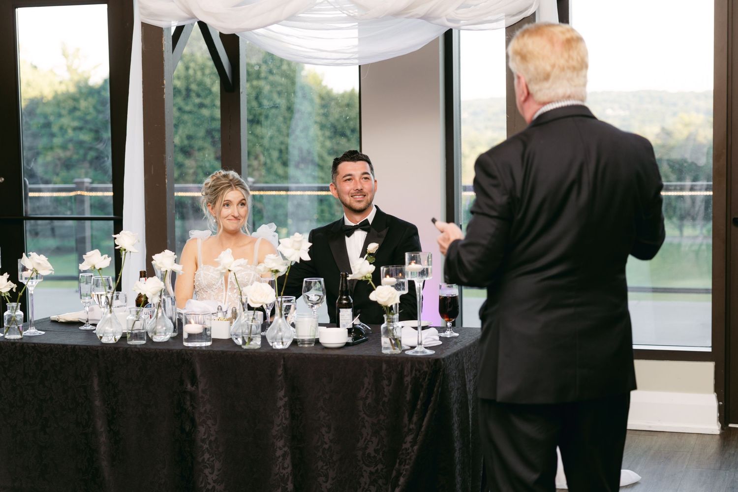 Wedding reception venue with elegant table settings and large windows overlooking a scenic landscape at dusk.