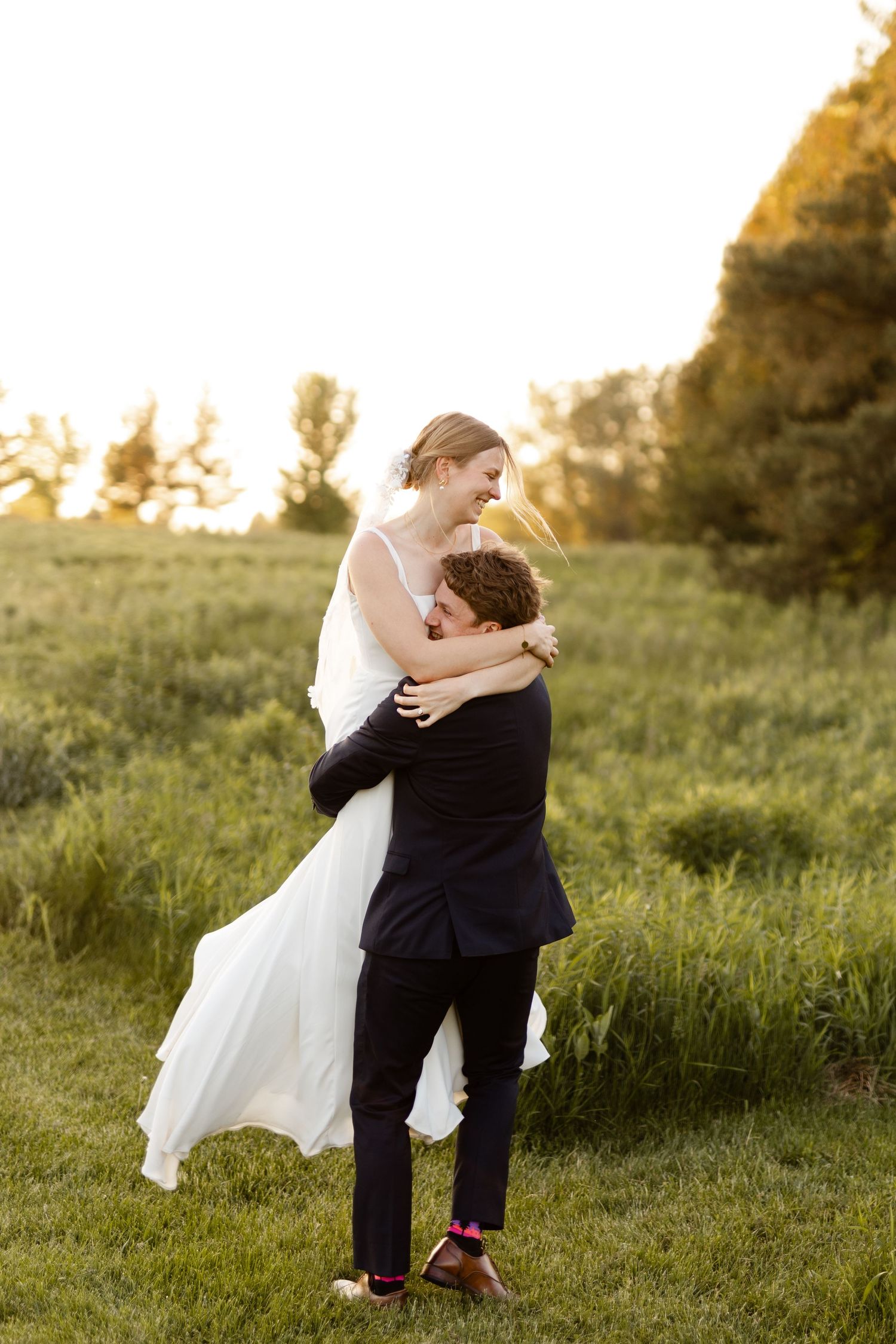 Tender moment between newlyweds during sunset photo session in a meadow.