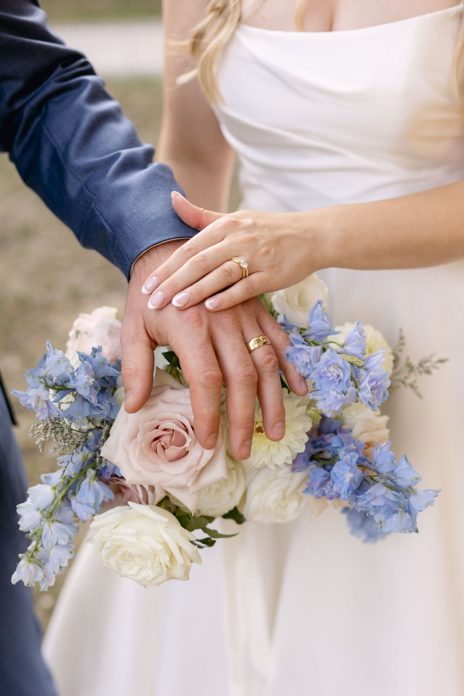 Close-up of wedding rings and bouquet with white roses and blue flowers.