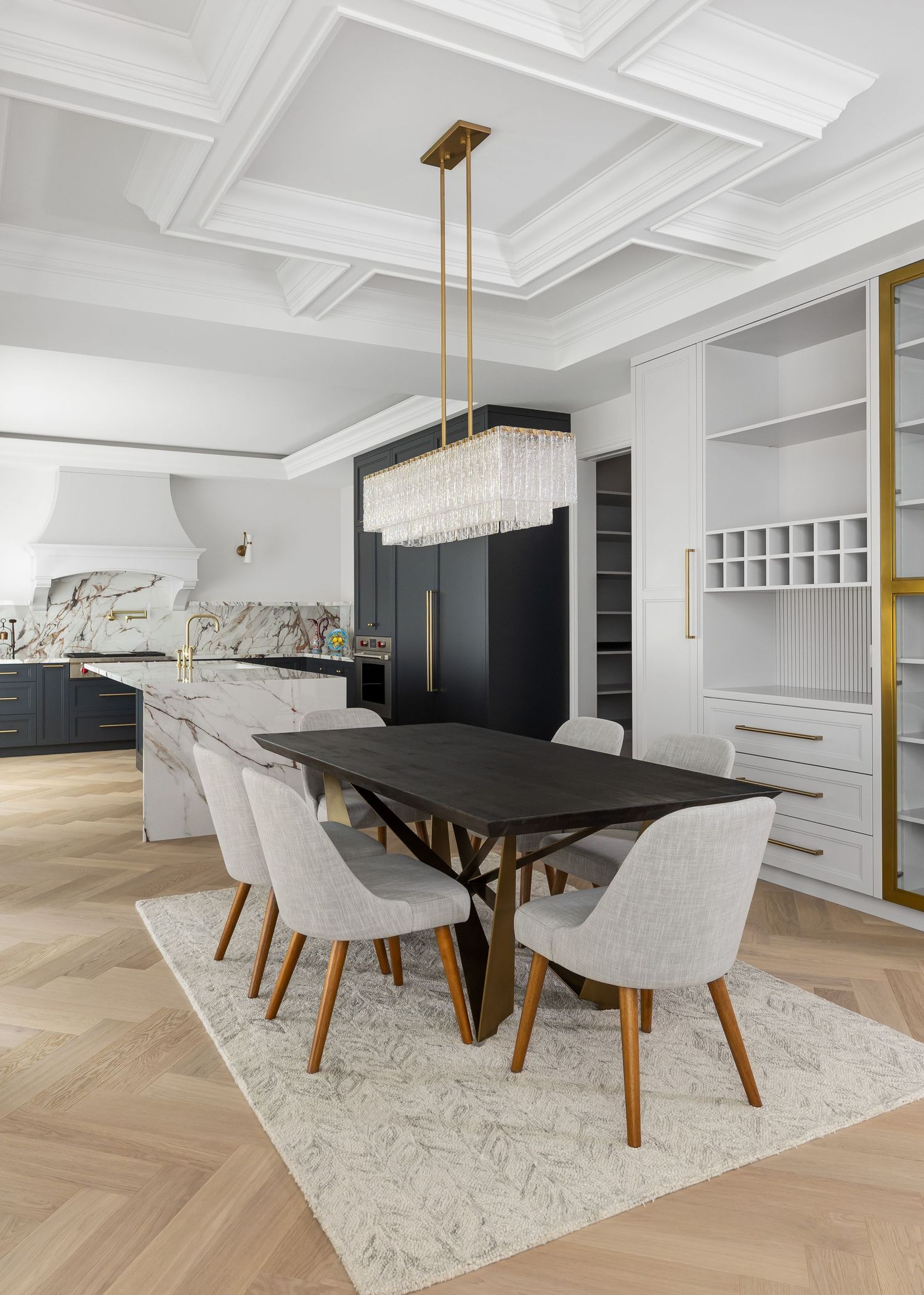 Sophisticated dining area with black table, white chairs, and crystal chandelier under coffered ceiling.