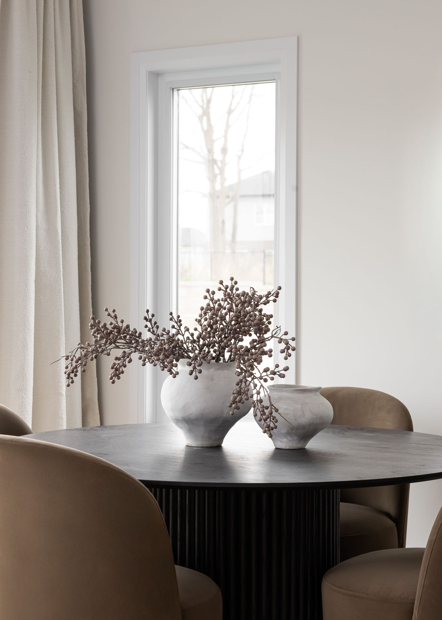 Elegant dining space with black table, taupe chairs and decorative dried flowers in vase.